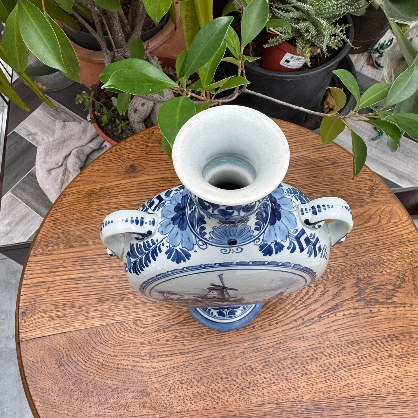 Blue and white ceramic vase on a wooden table with plants in the background
