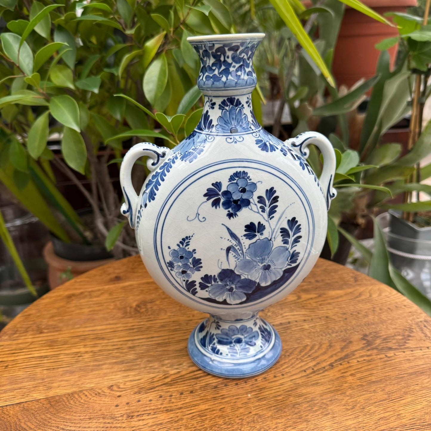 Blue and white floral-patterned vase on a wooden surface with green plants in the background