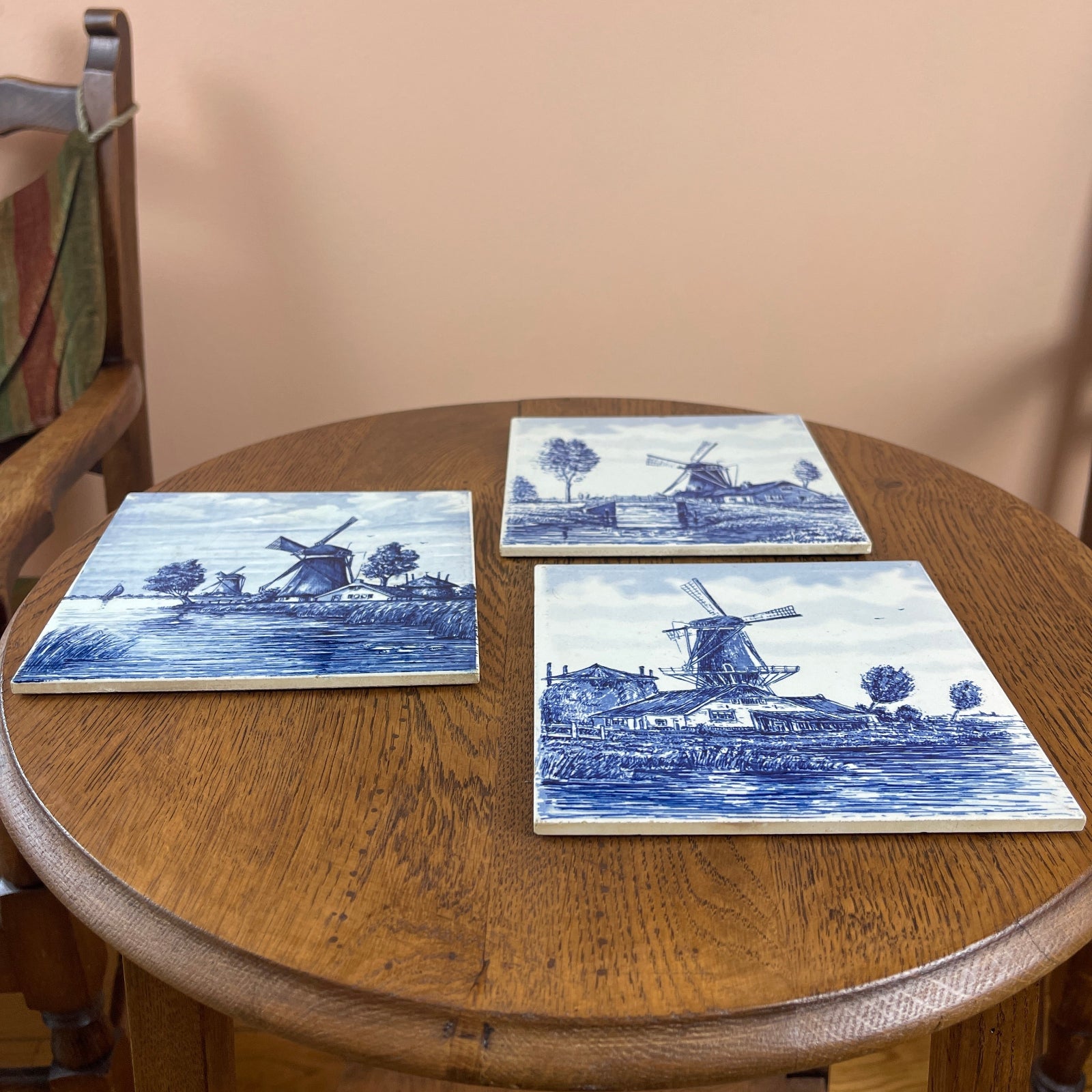 Three blue and white ceramic tiles with windmill designs on a wooden table.
