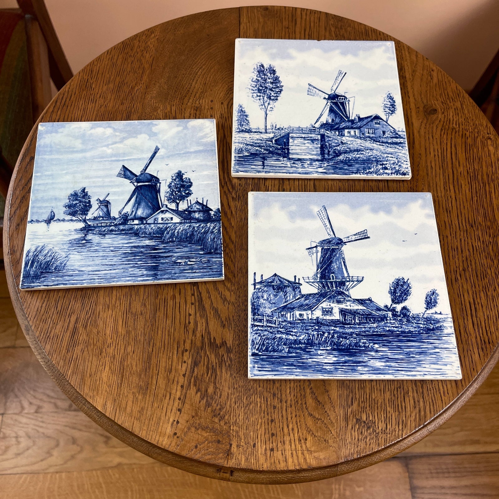 Three blue and white ceramic tiles with windmill designs on a wooden table.