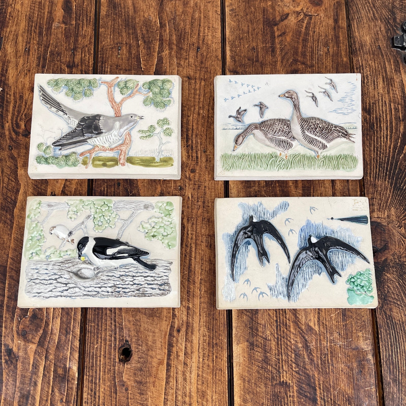 Four ceramic tiles with bird illustrations on a wooden surface