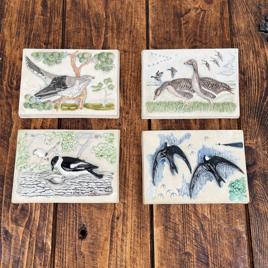 Four ceramic tiles with bird illustrations on a wooden surface