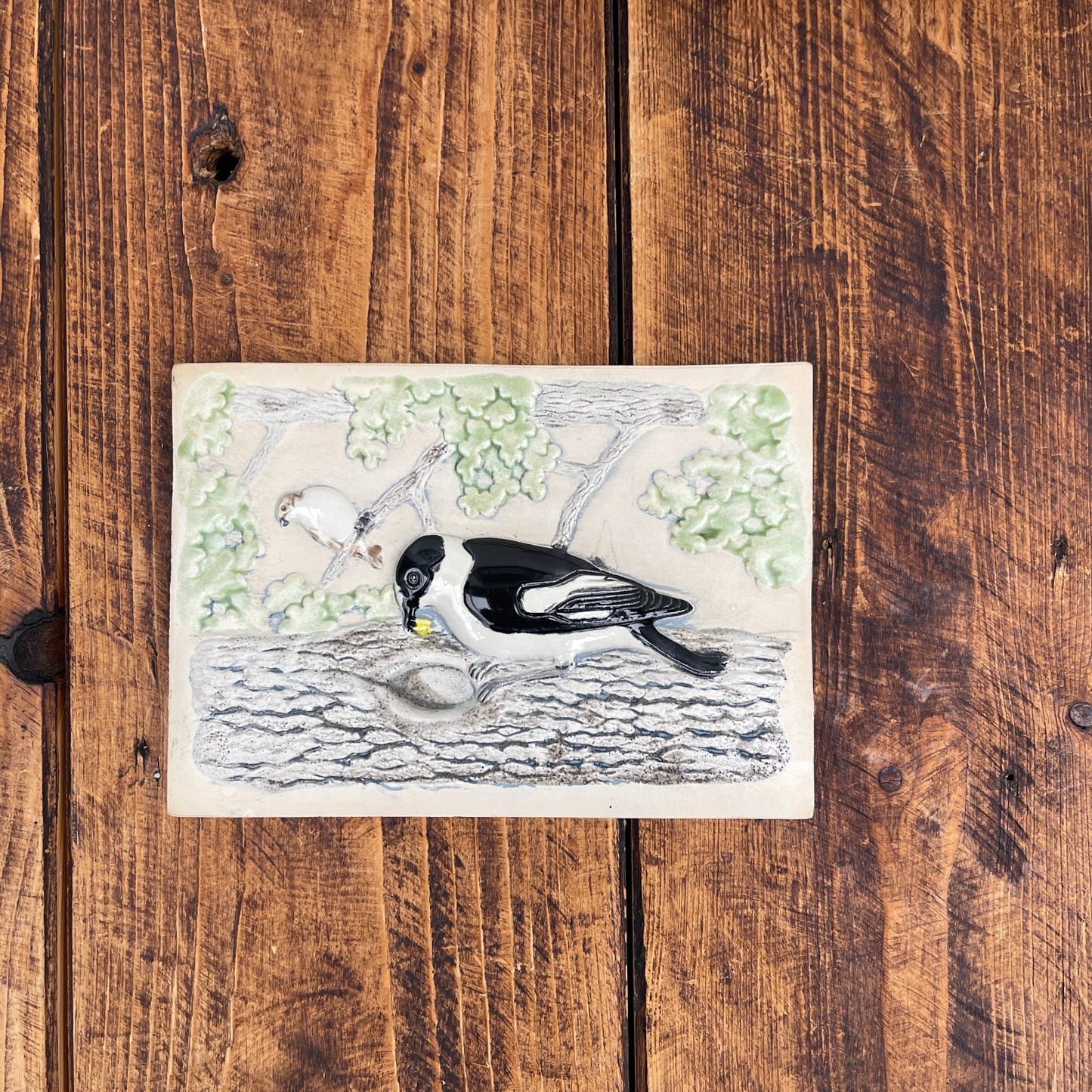 Illustration of a bird on a branch with leaves, placed on a wooden surface.