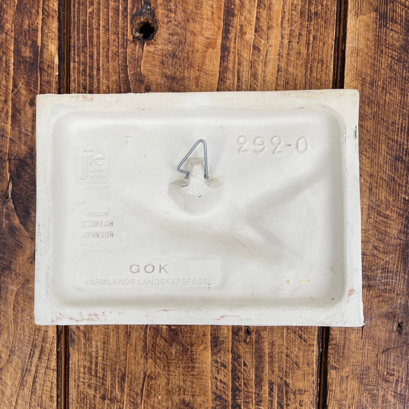 White rectangular plastic component with a hook on a wooden surface