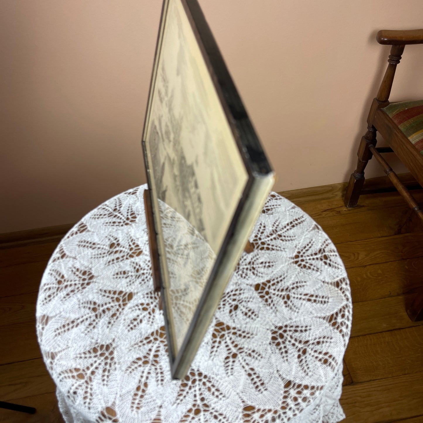 Framed picture on a lace tablecloth with a wooden chair in the background