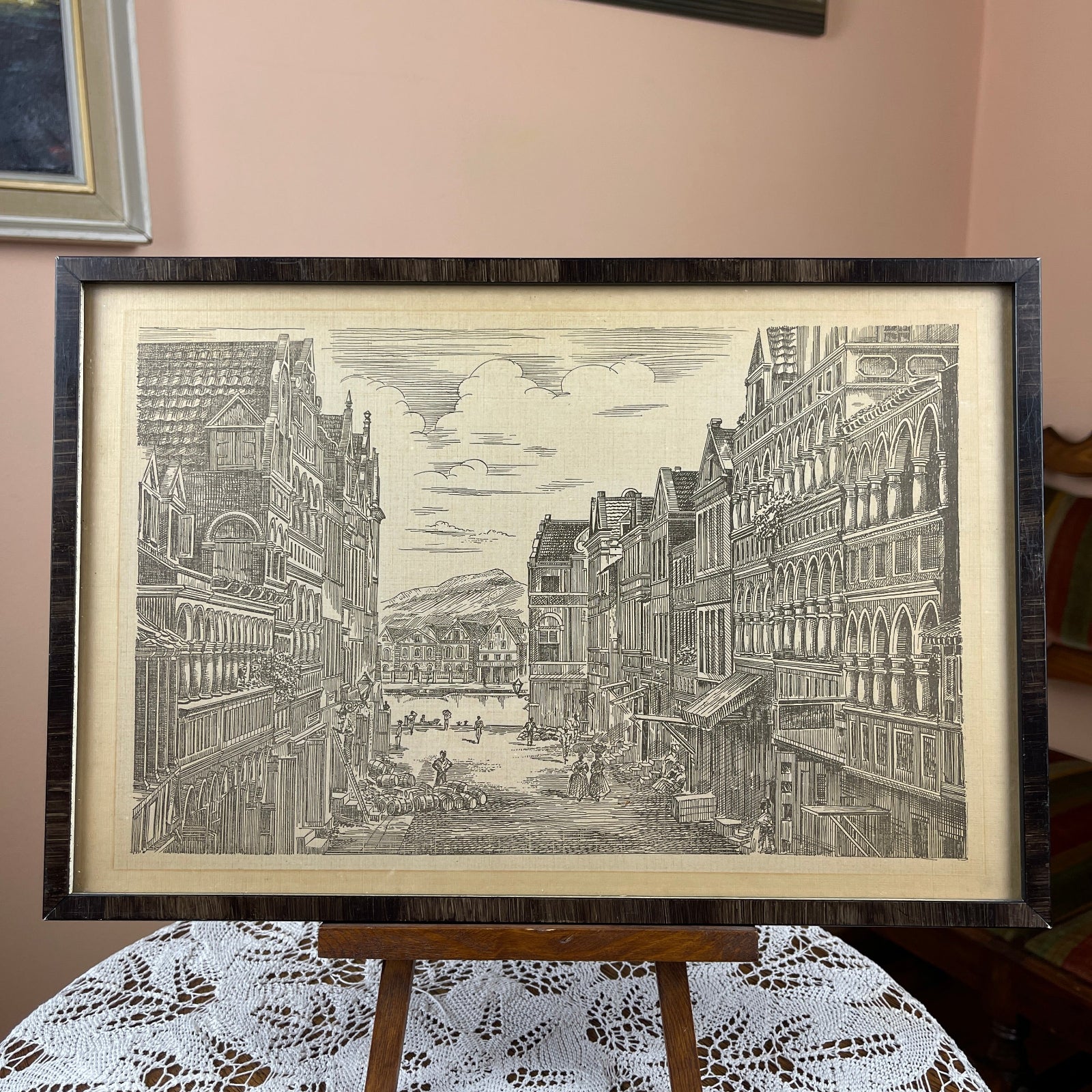 Framed black and white print of a city scene on a table with lace tablecloth.