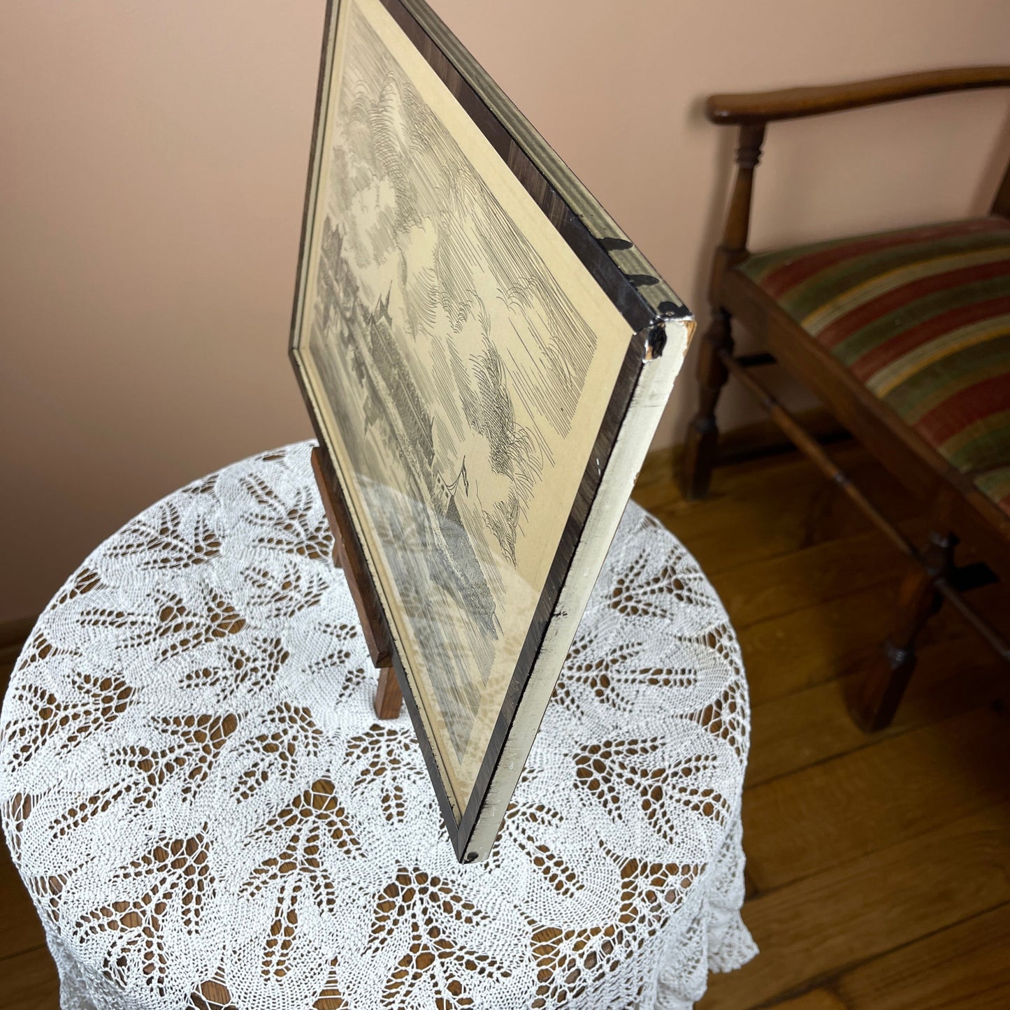 Framed artwork on a lace tablecloth with a wooden chair in the background