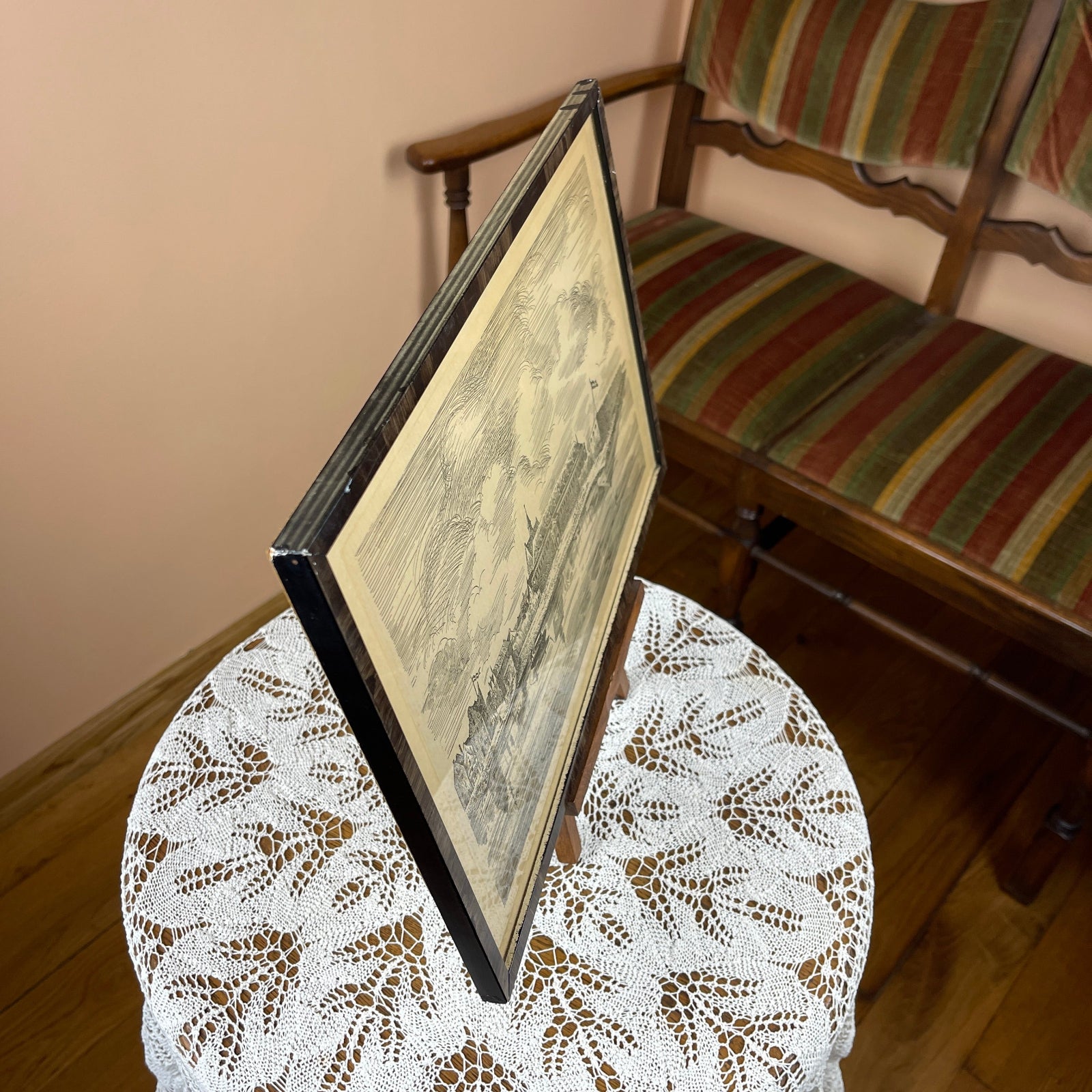 Framed antique map on a small table with a striped chair in the background