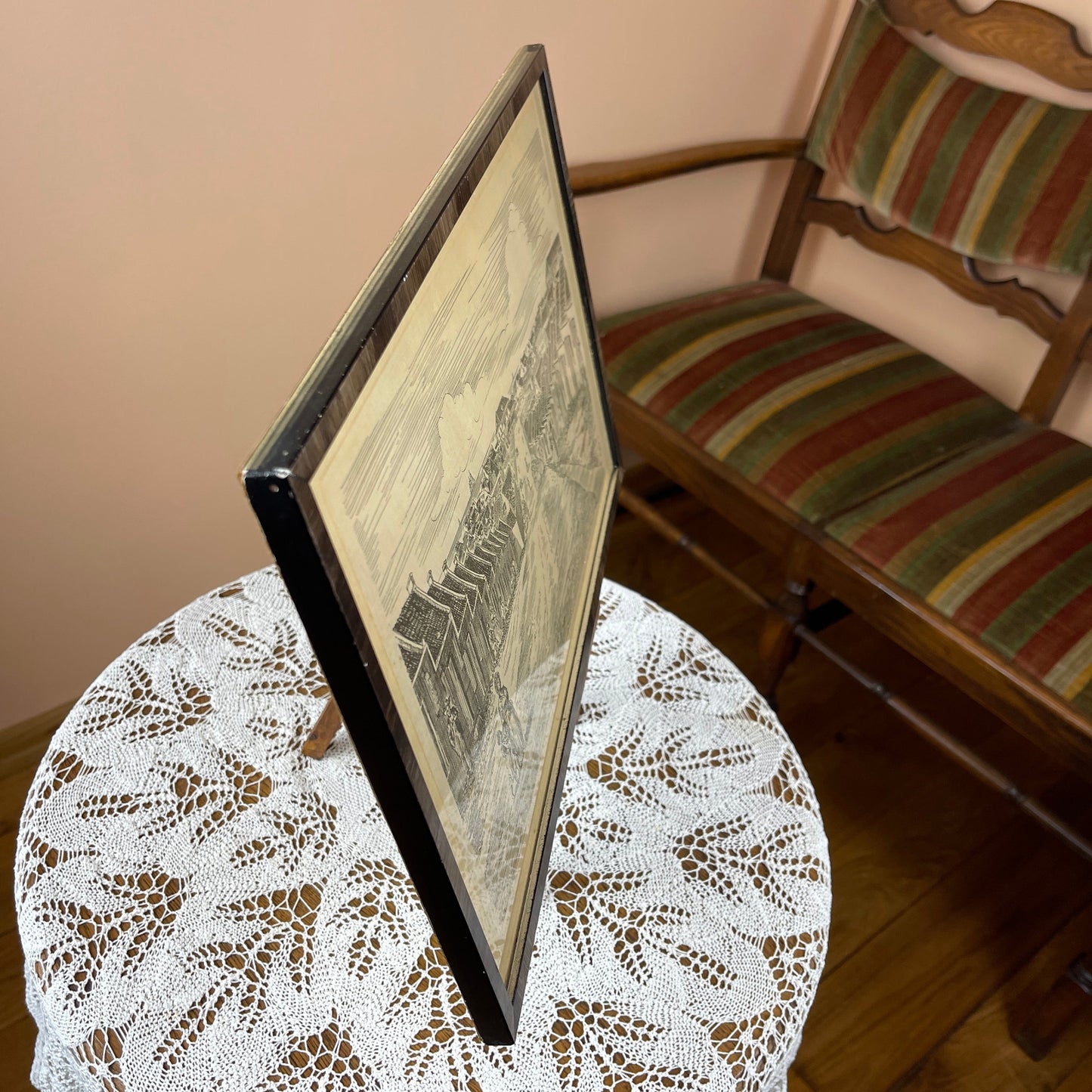 Framed artwork on a lace tablecloth with a striped chair in the background