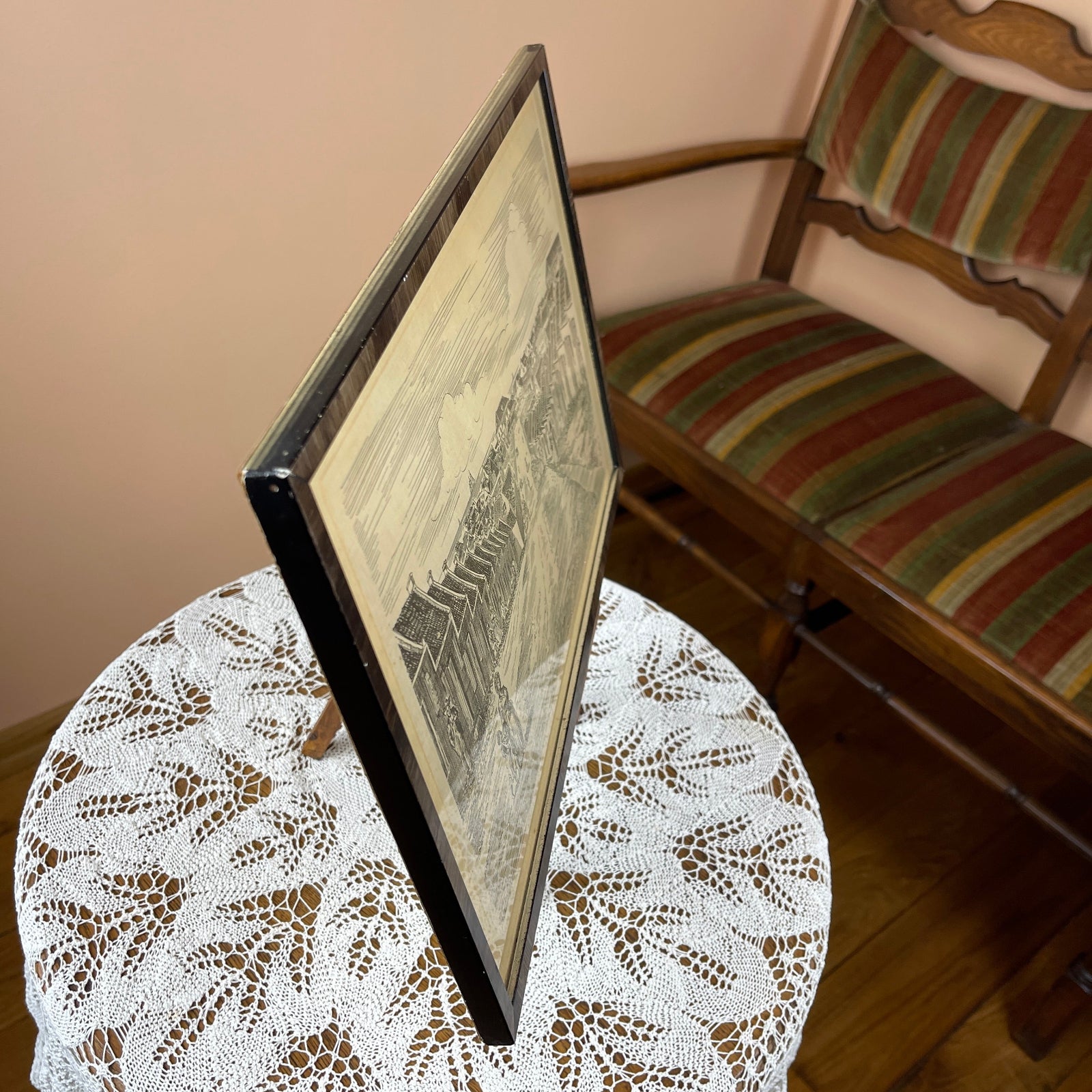 Framed artwork on a lace tablecloth with a striped chair in the background