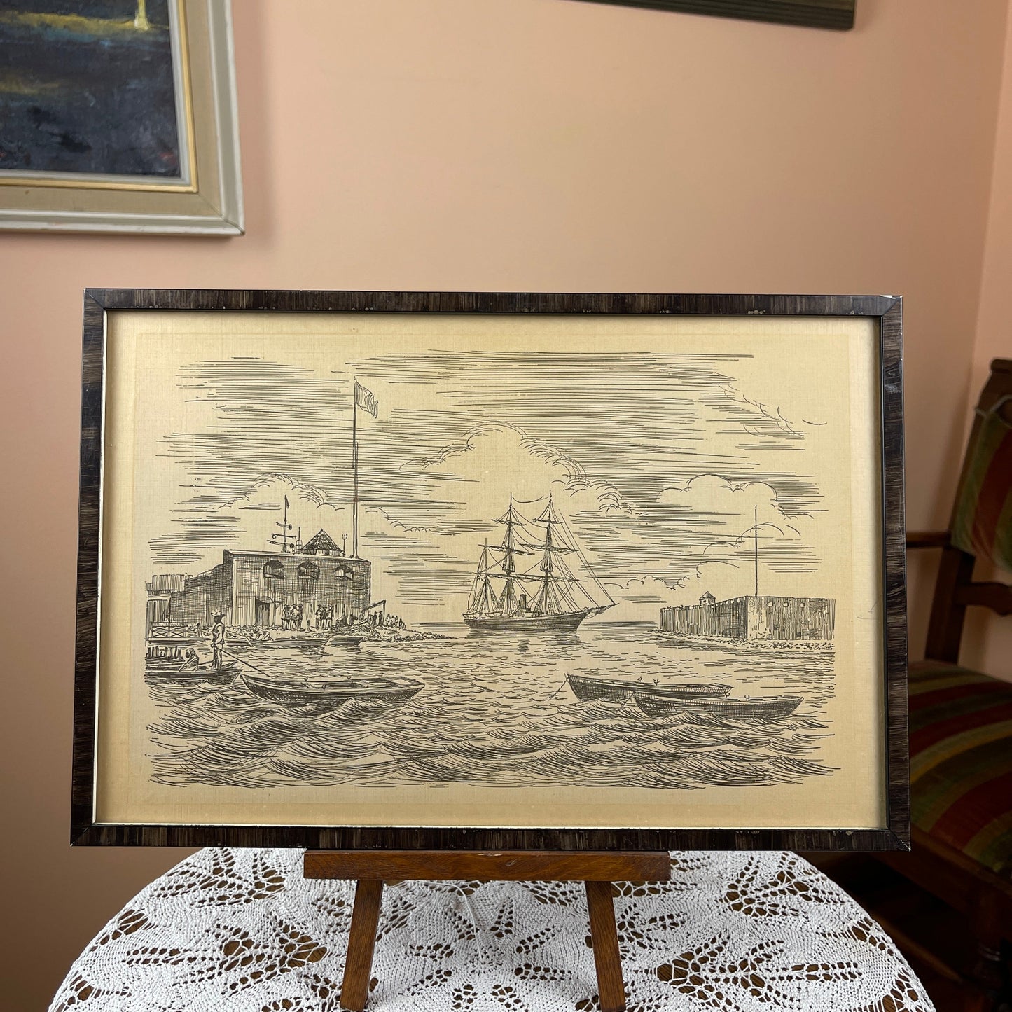 Framed black and white print of a ship on water with buildings in the background, displayed on a table.