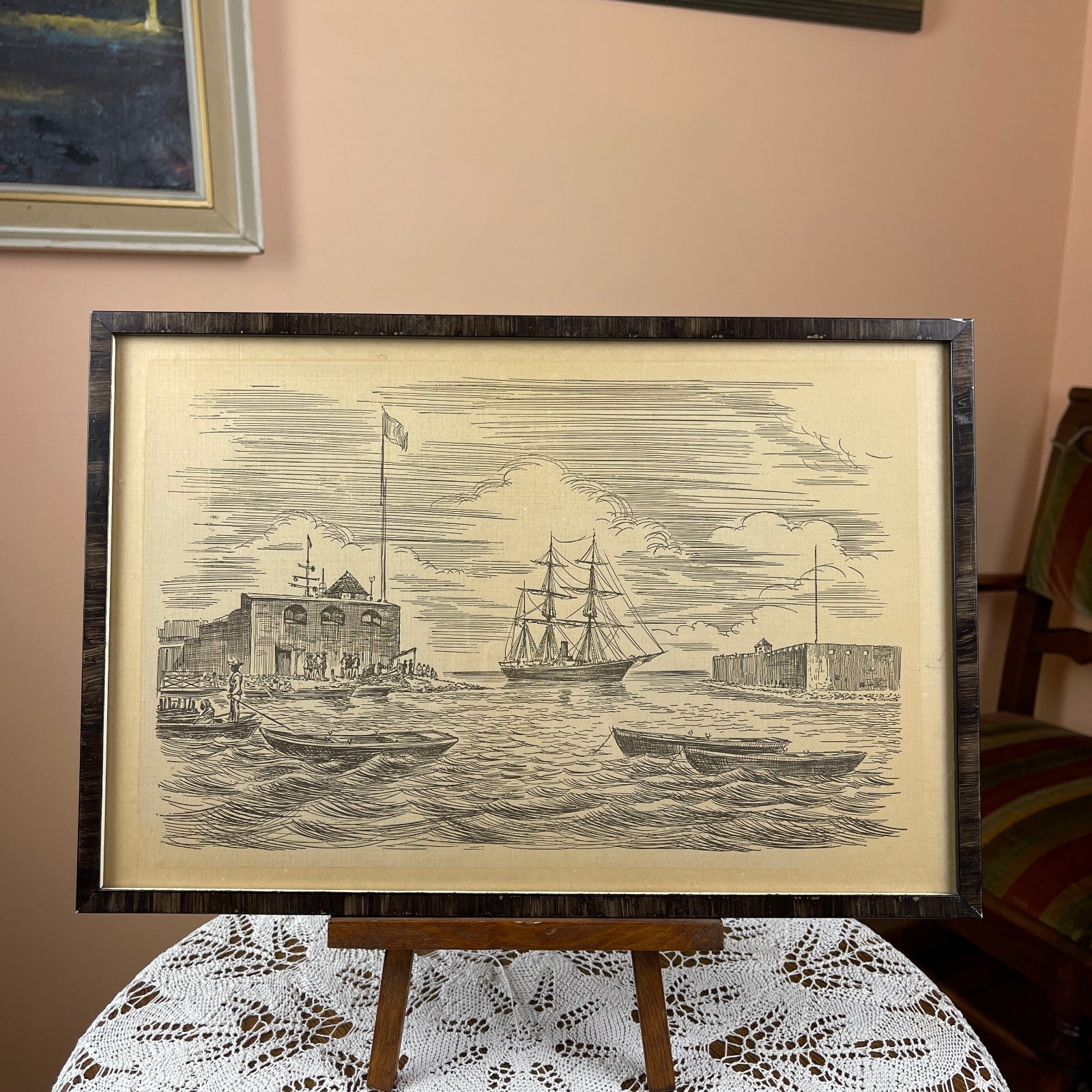 Framed black and white print of a ship on water with buildings in the background, displayed on a table.