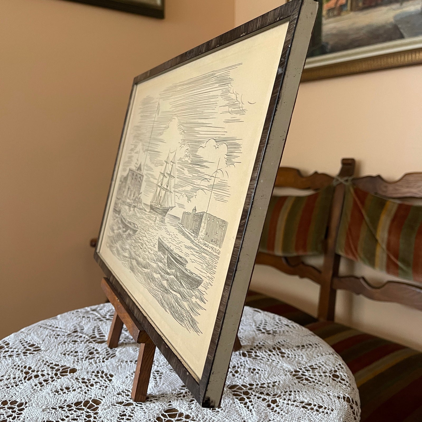 Framed black and white print on a small easel with a striped chair in the background