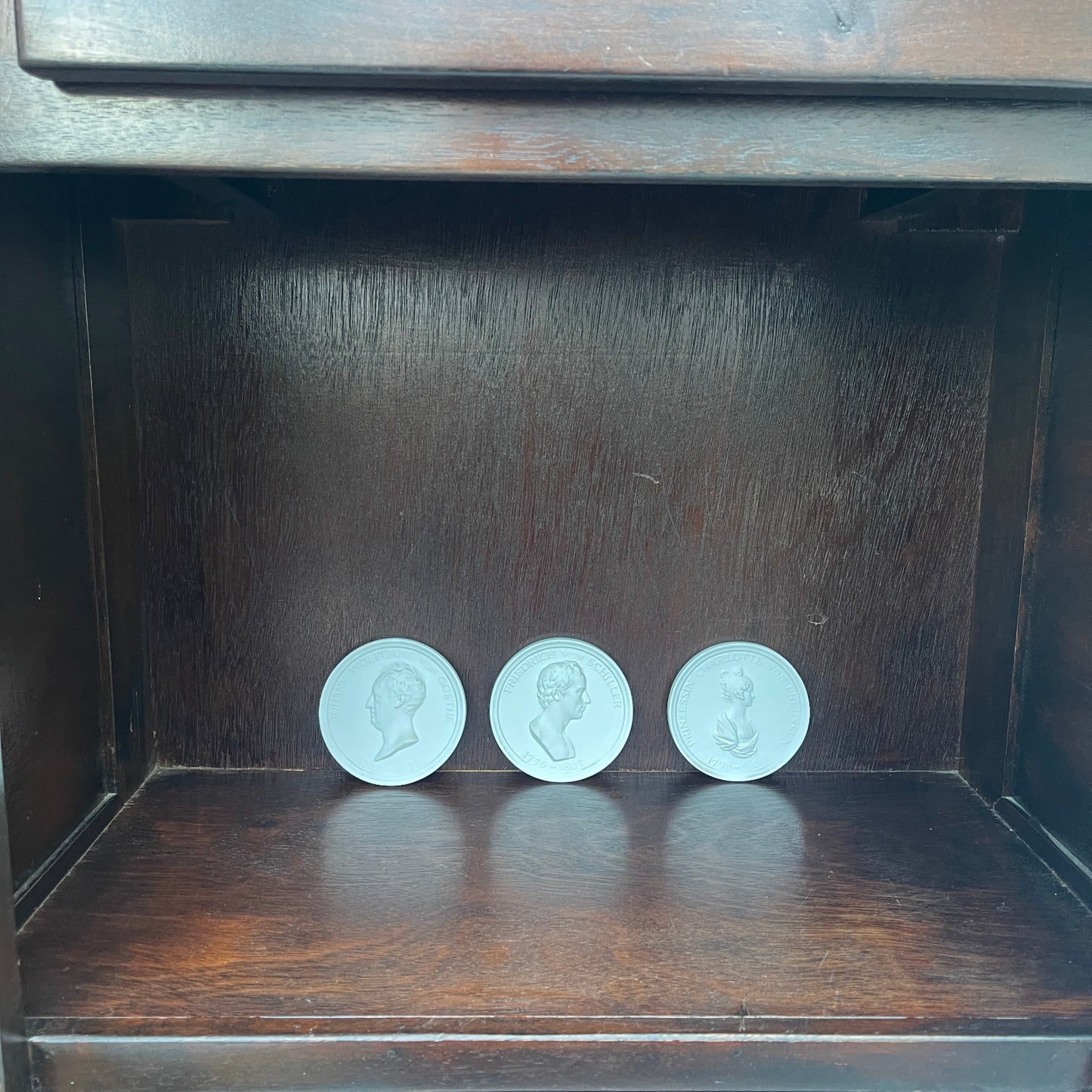 Three circular objects with engraved faces on a wooden shelf