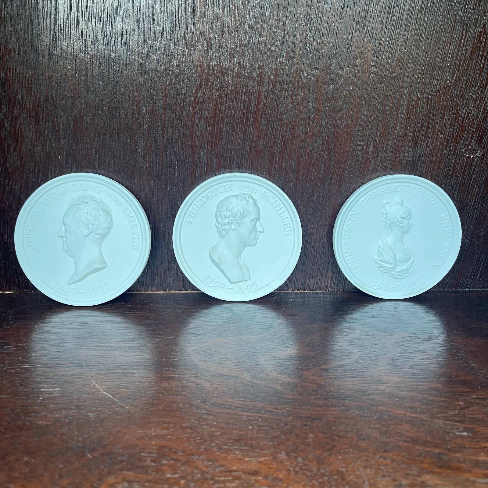 Three light blue coins with embossed portraits on a dark wooden surface