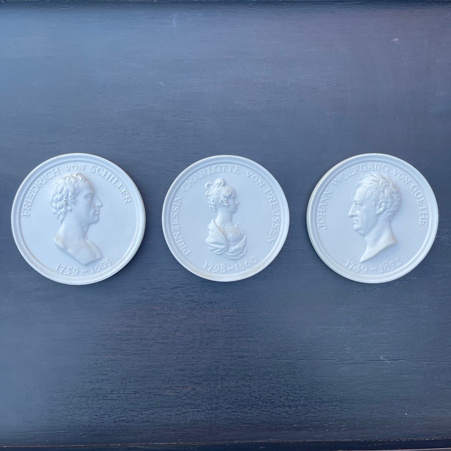 Three white coins with embossed portraits on a dark blue surface