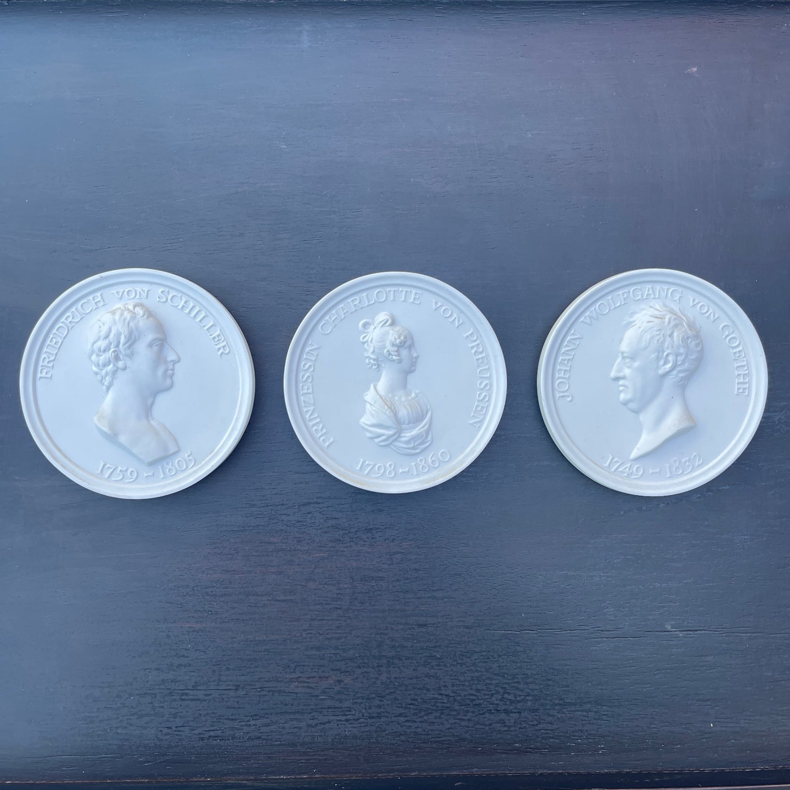 Three white coins with embossed portraits on a dark blue surface