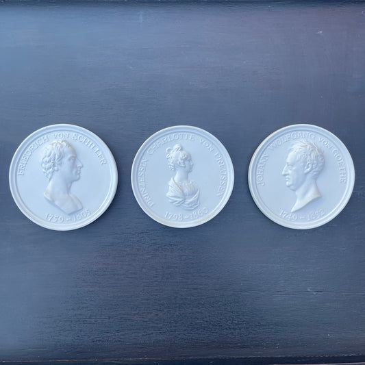 Three white coins with embossed portraits on a dark blue surface