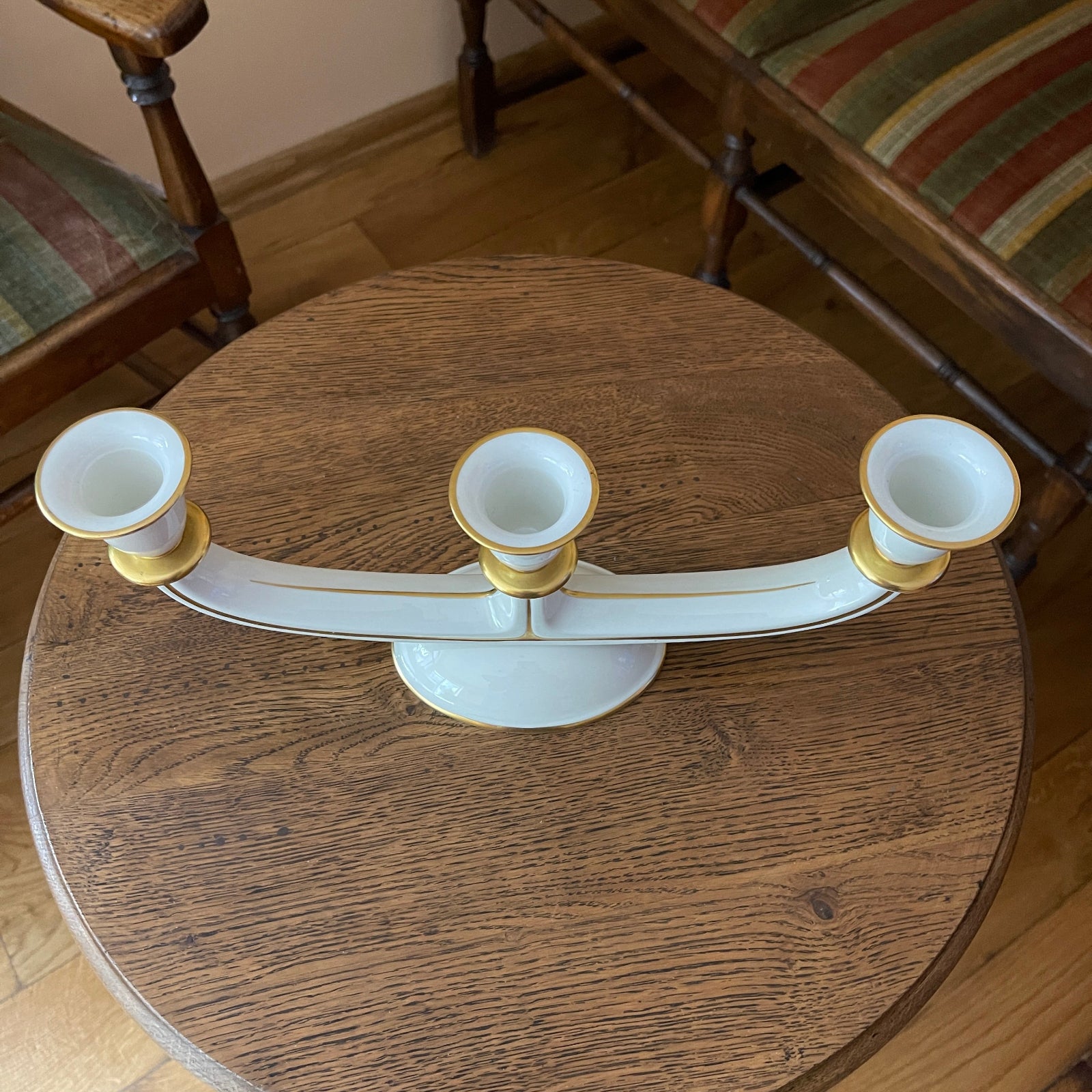 Decorative white and gold candle holder on a wooden table with chairs in the background.
