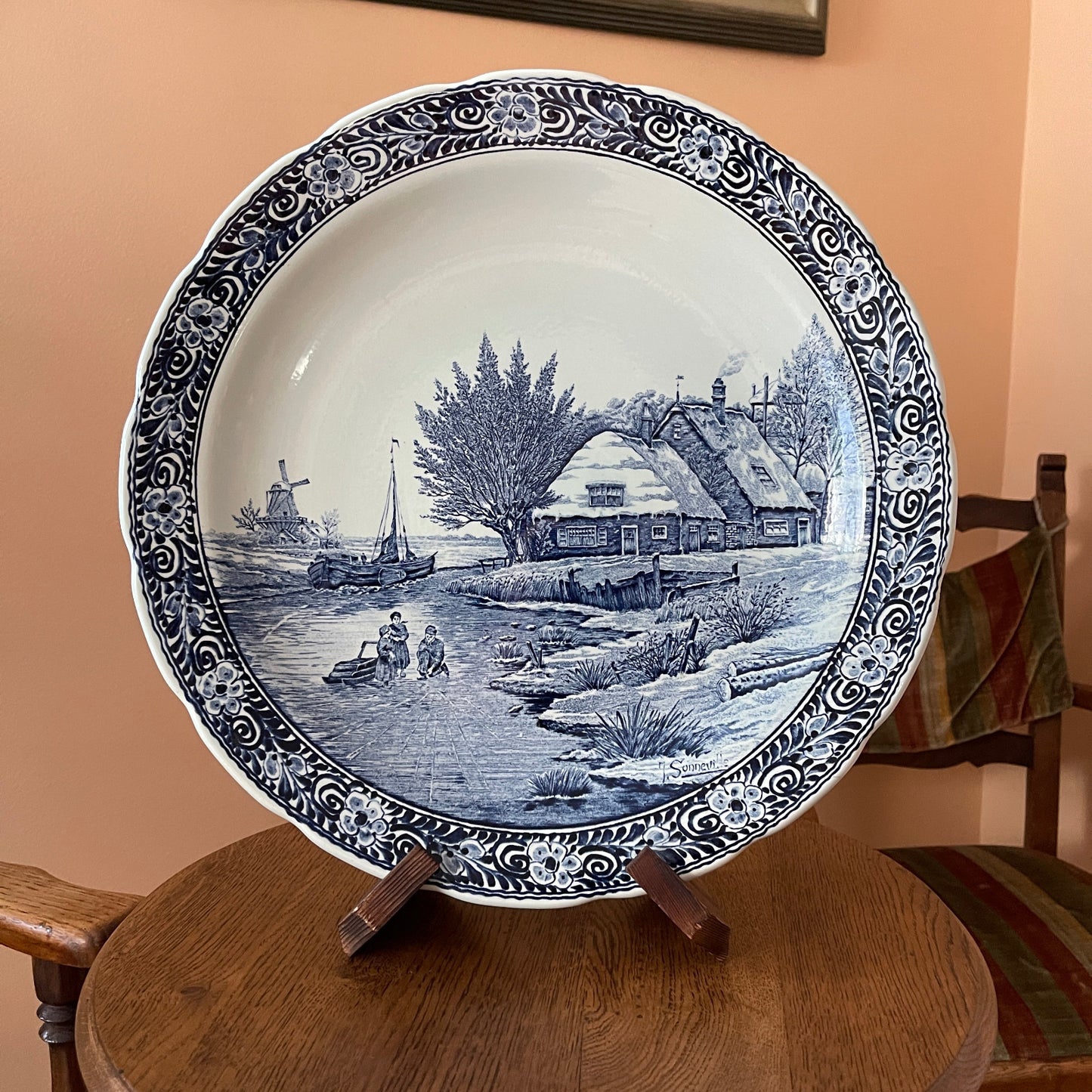 Decorative plate with a blue and white landscape design on a wooden stand against a beige wall.