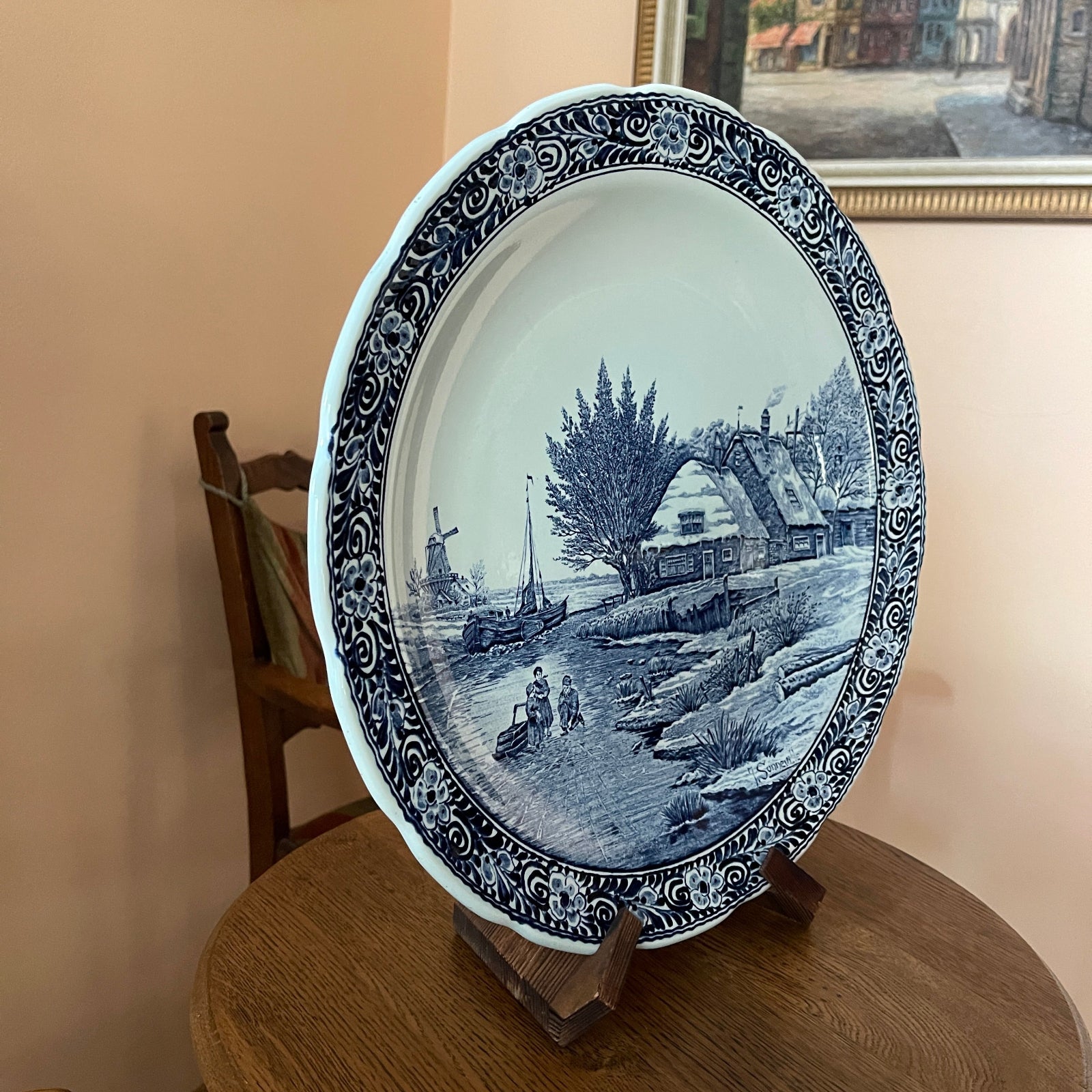Decorative plate with a blue and white scene on a wooden stand against a beige wall.
