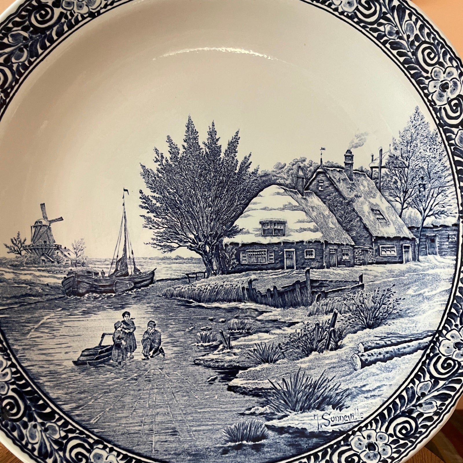 Decorative plate with a black and white landscape design featuring a house, windmill, and people by a stream.