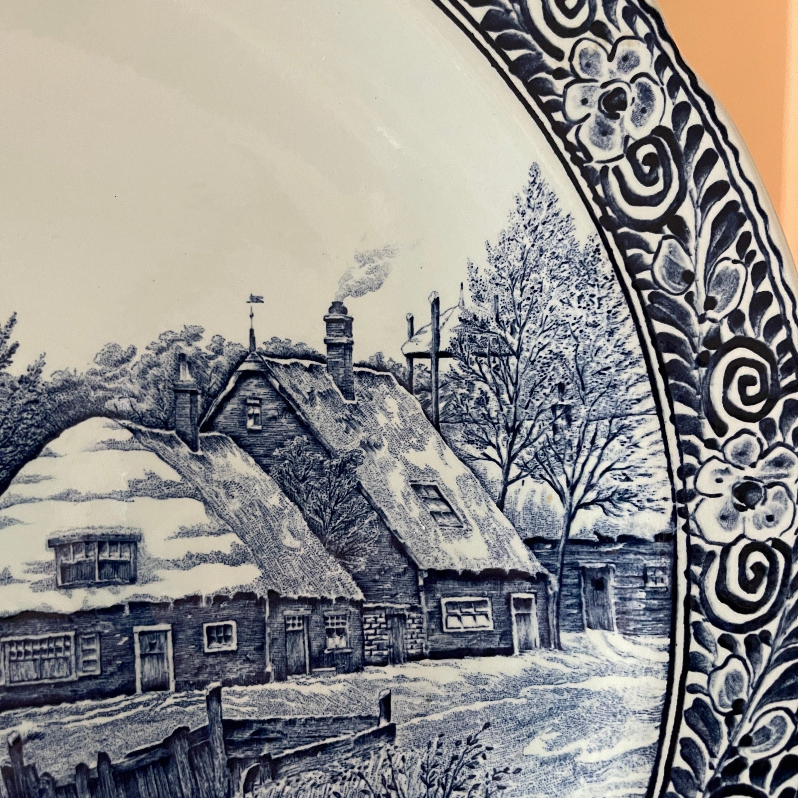 Decorative tile with a winter scene of a house and trees, framed by ornate blue patterns.