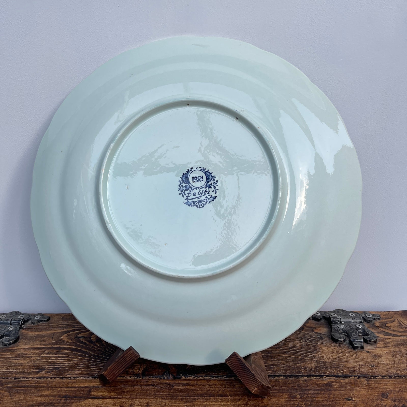 White ceramic plate with a blue emblem on a wooden stand against a light purple background