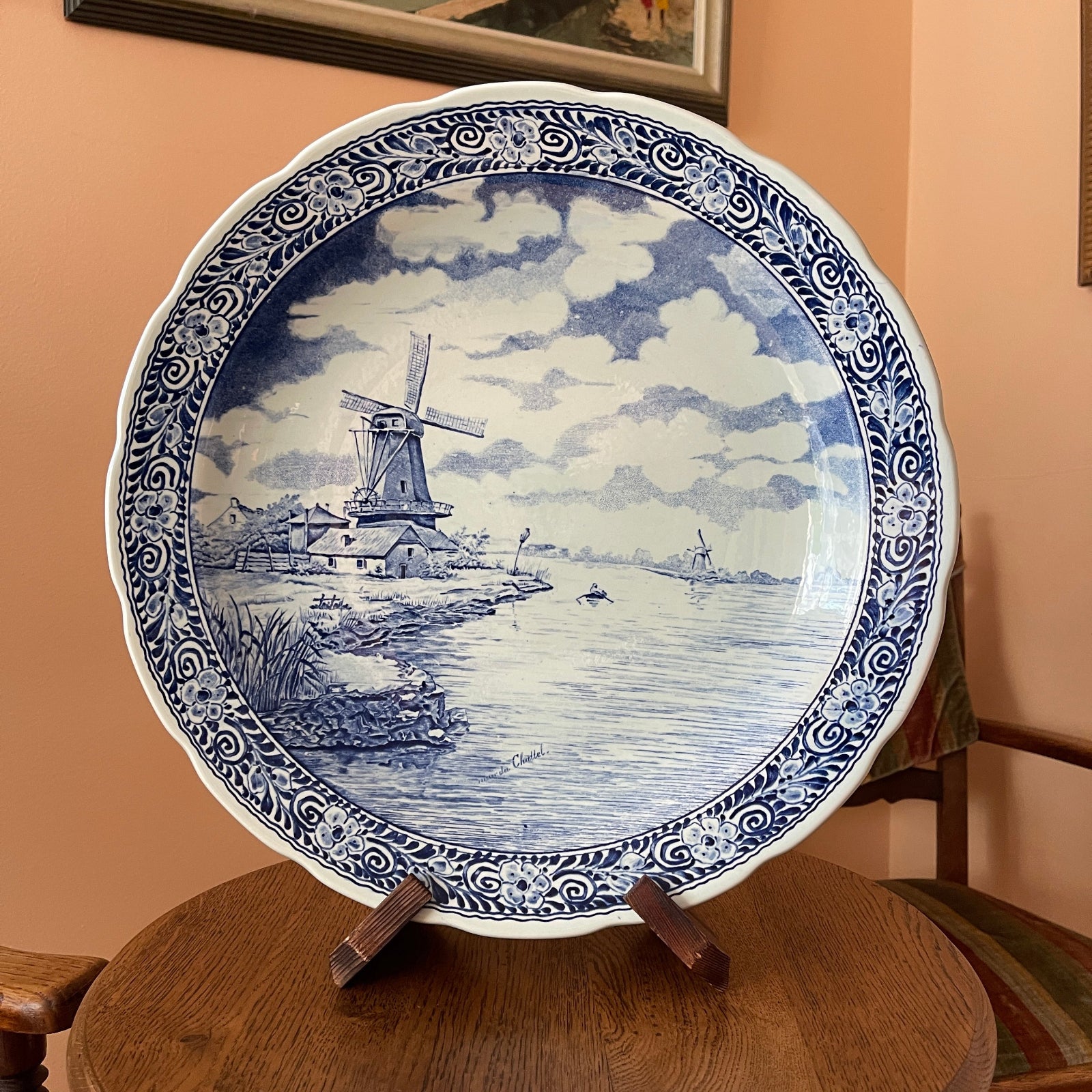 Decorative plate with a windmill design on a wooden stand against a beige wall.