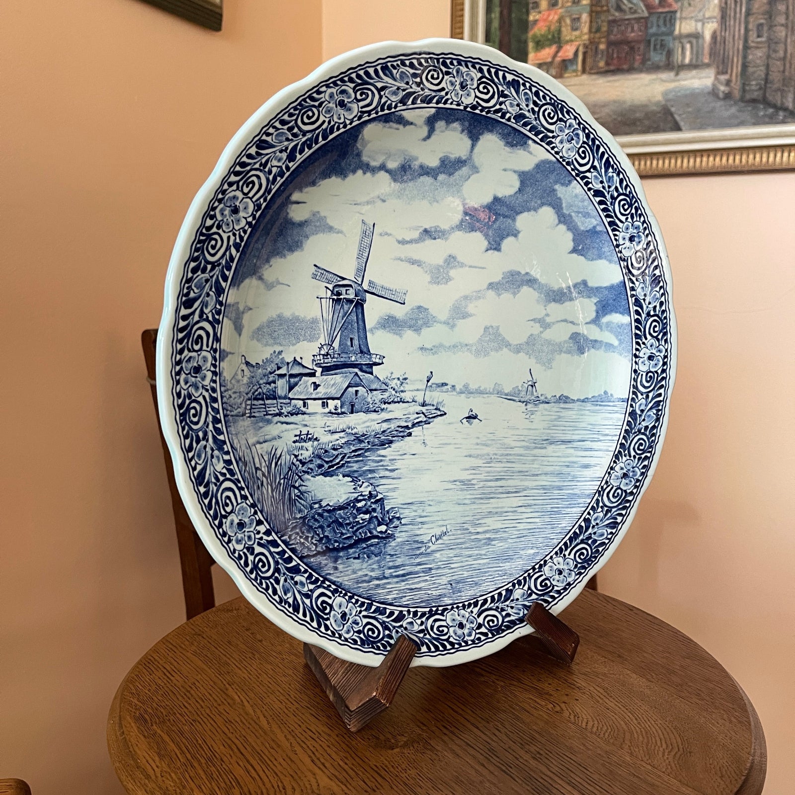 Decorative plate with blue and white design of a windmill on a stand against a beige wall.
