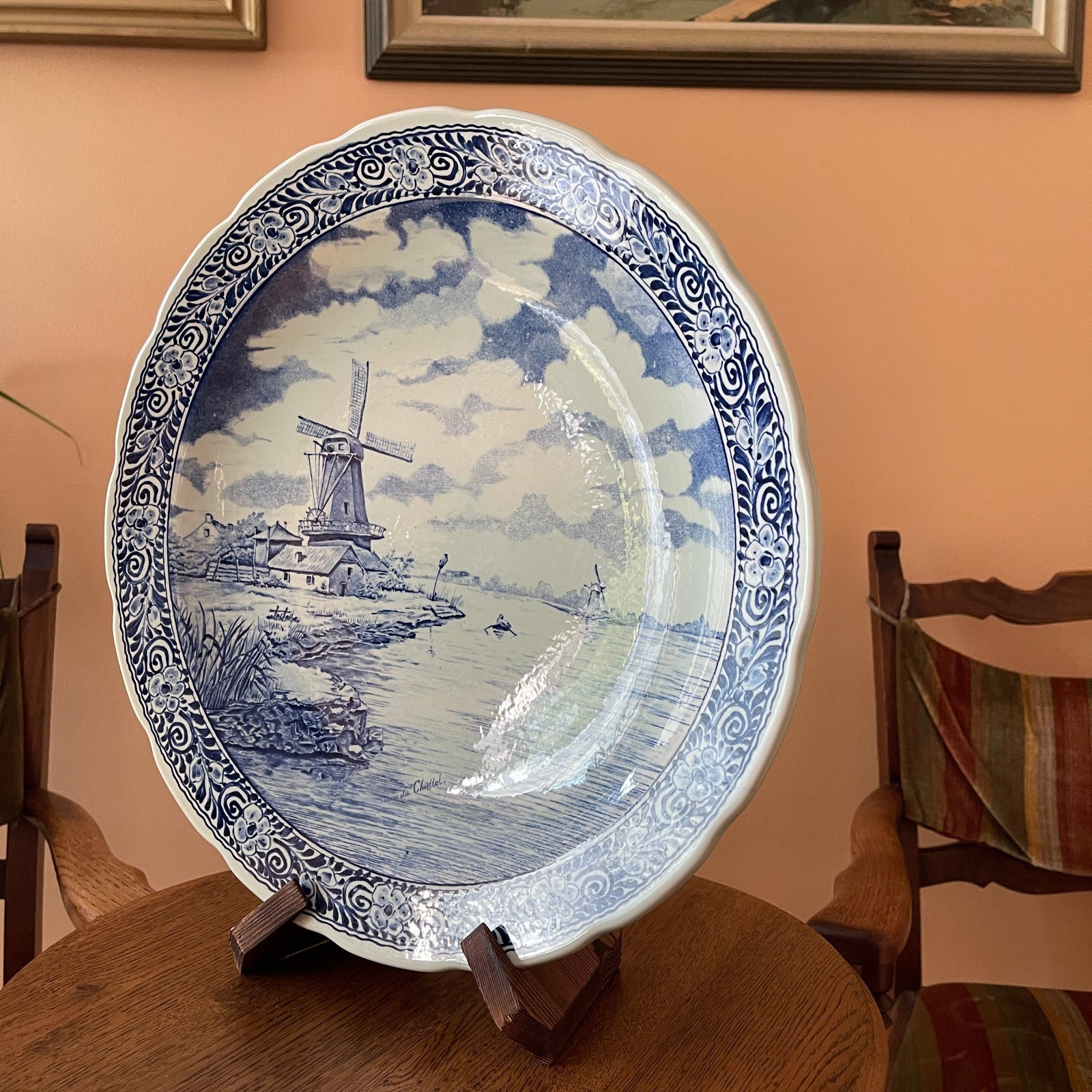 Decorative plate with a blue and white design of a windmill on a wooden stand.