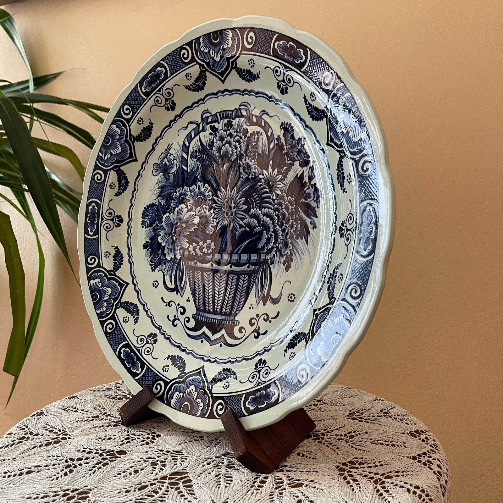 Decorative ceramic plate with floral design on a stand against a beige wall.