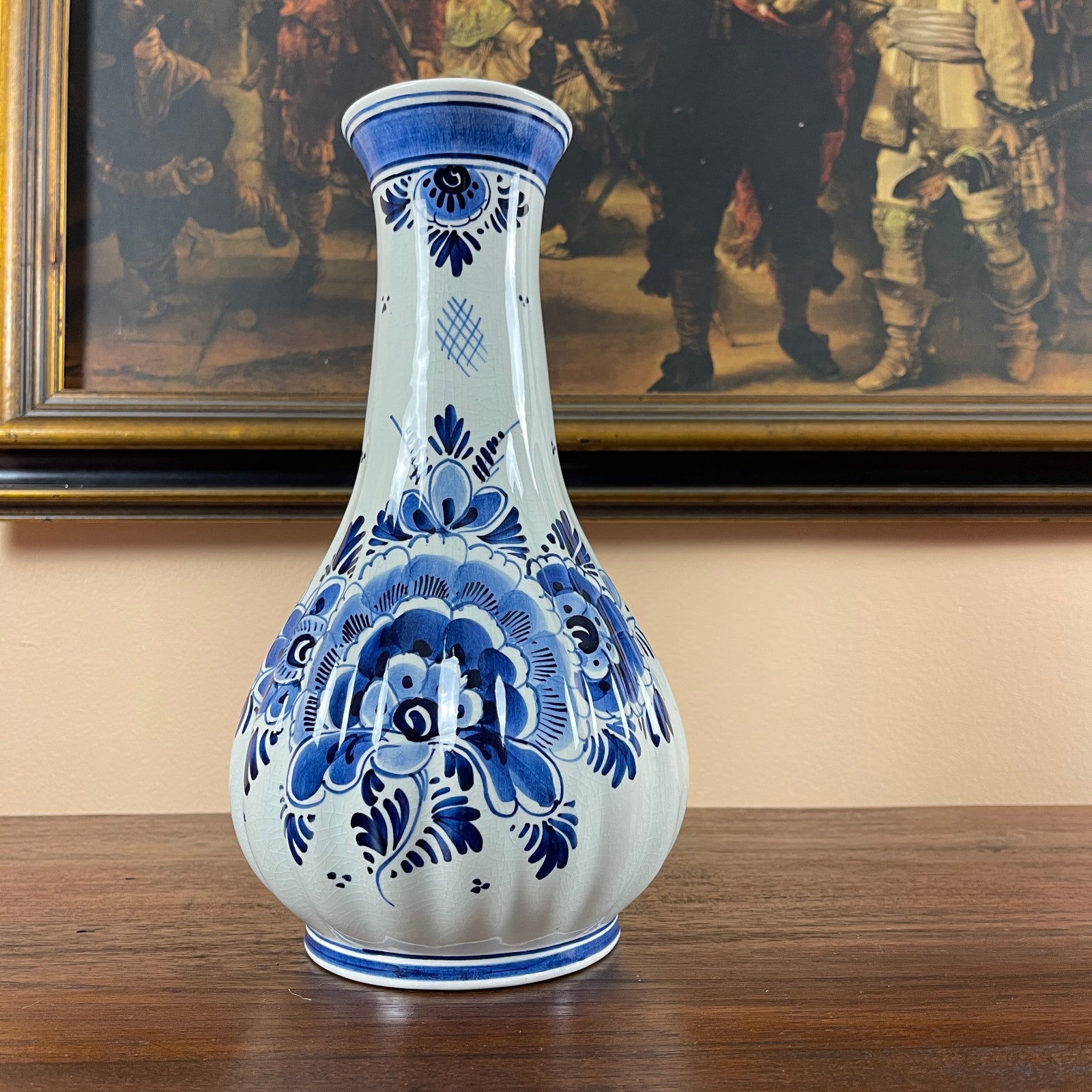 Blue and white decorative vase on a wooden surface with a painting in the background
