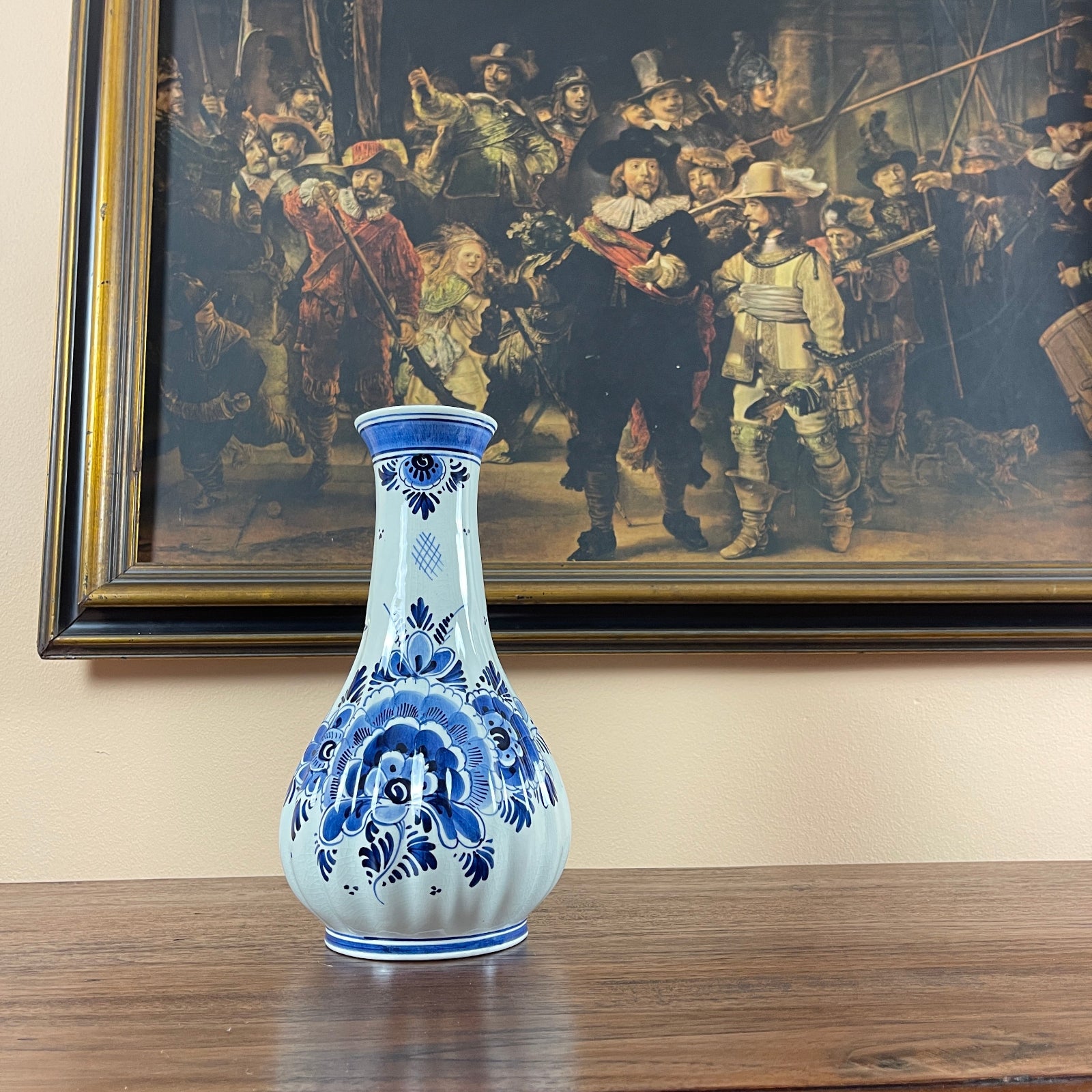 Blue and white decorative vase on a wooden surface with a painting of historical figures in the background.