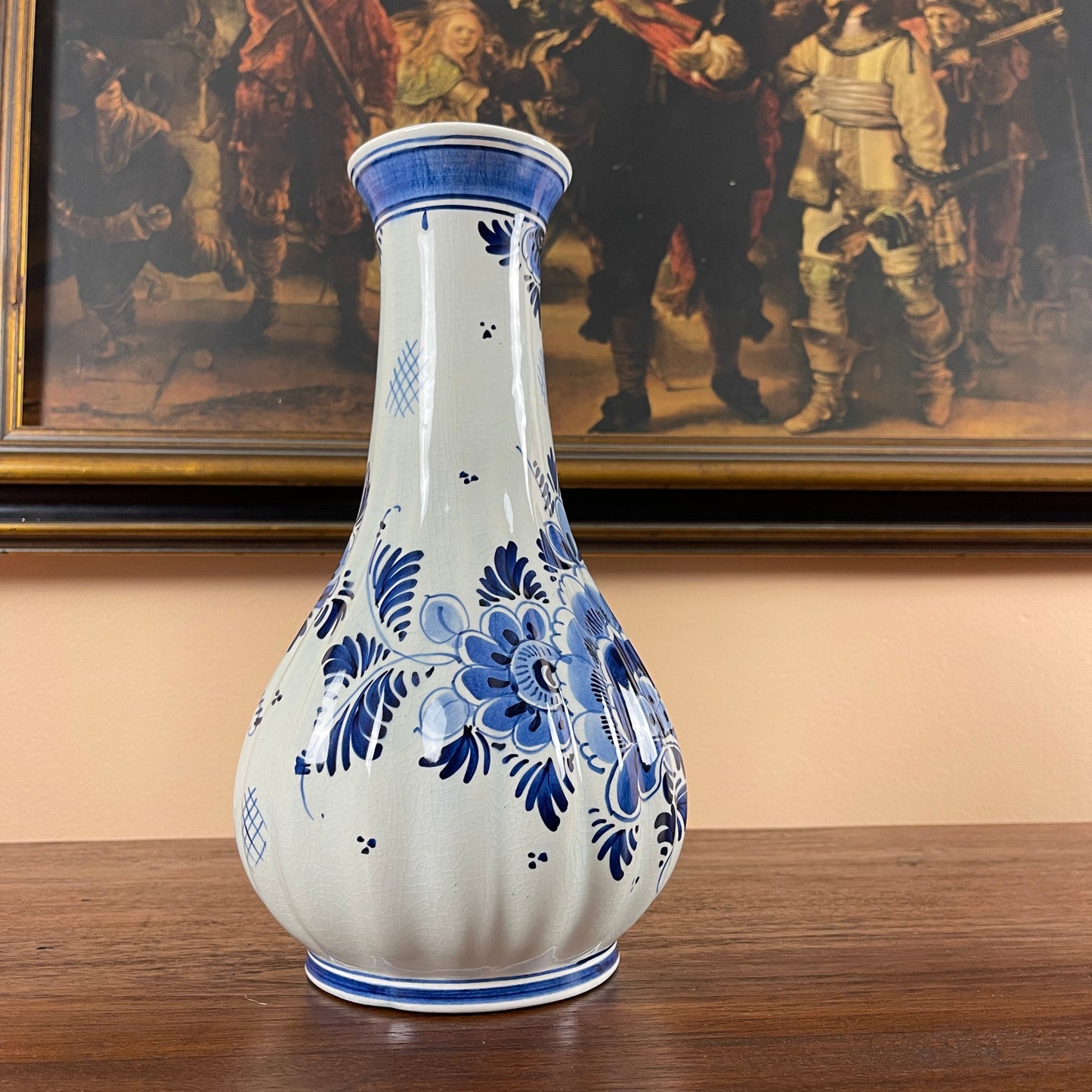 Ceramic vase with blue floral patterns on a wooden surface, framed painting in the background