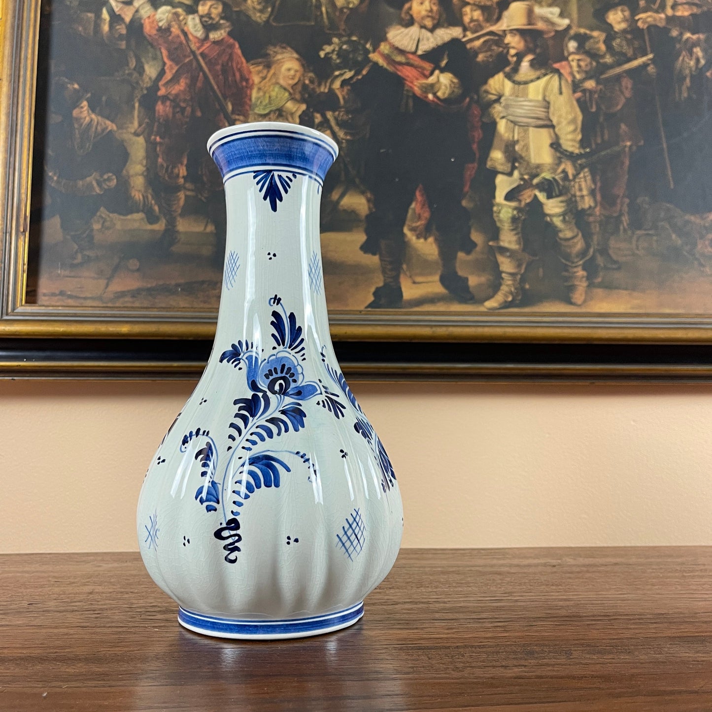 White vase with blue floral patterns in front of a painting of historical figures