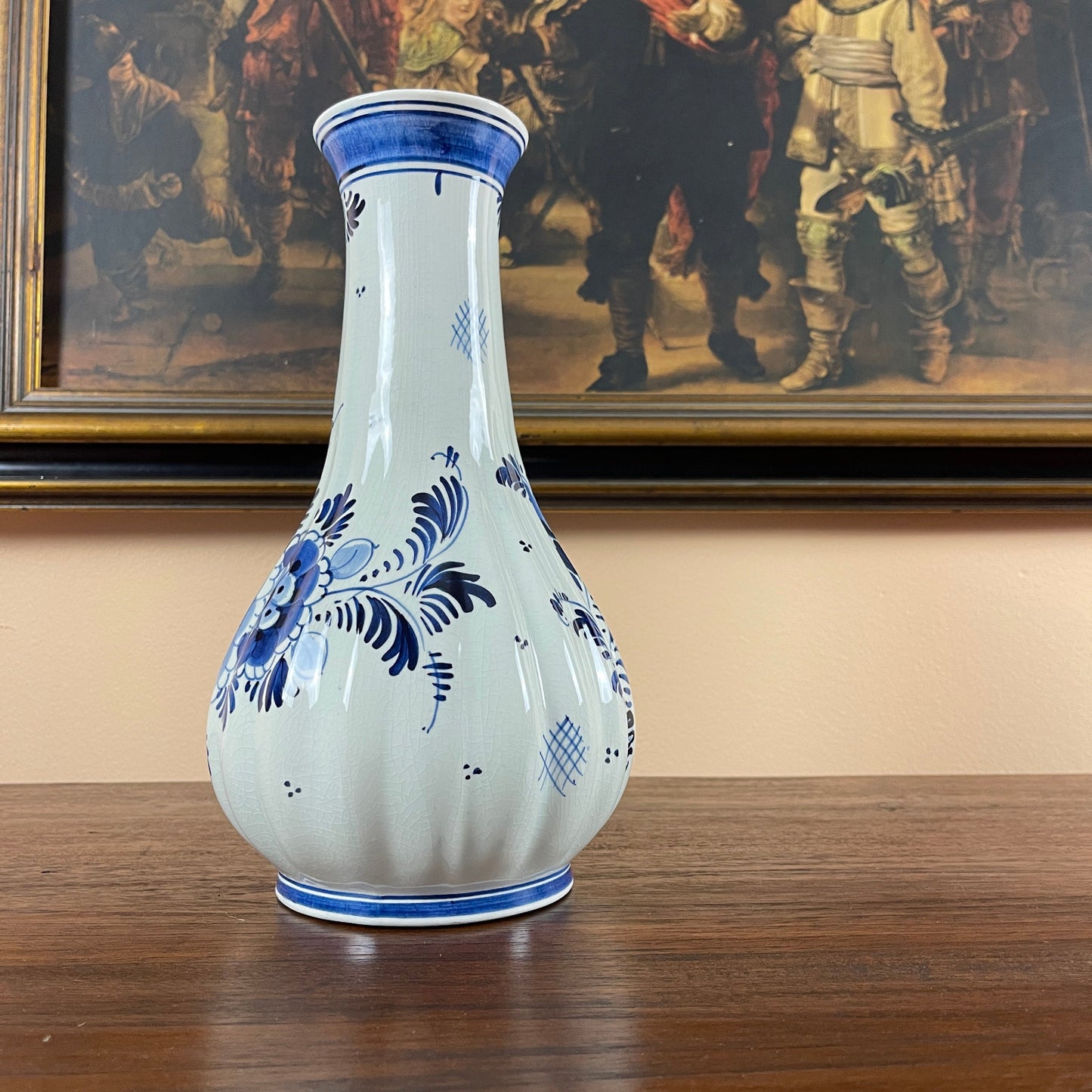 White ceramic vase with blue floral patterns on a wooden surface, framed artwork in the background