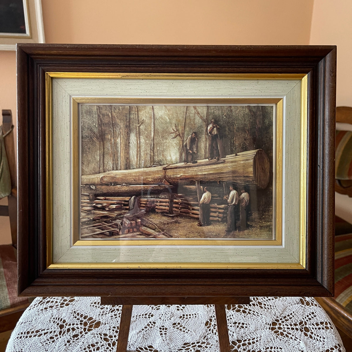 Framed artwork depicting a scene with logs and people in a forest setting.