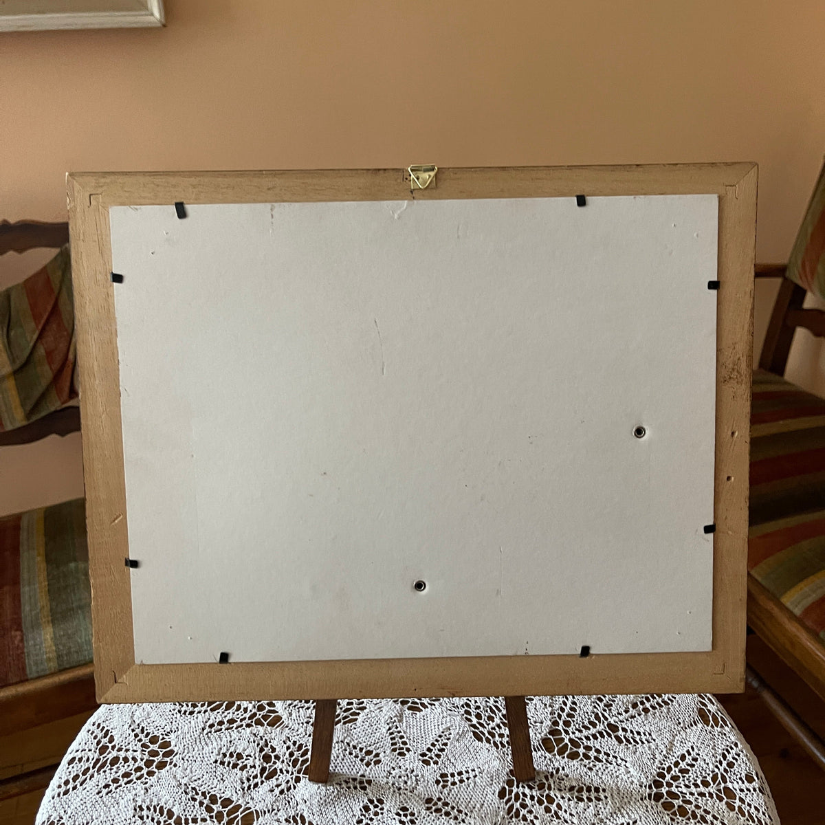 Back of a wooden picture frame with a white interior on a lace tablecloth.