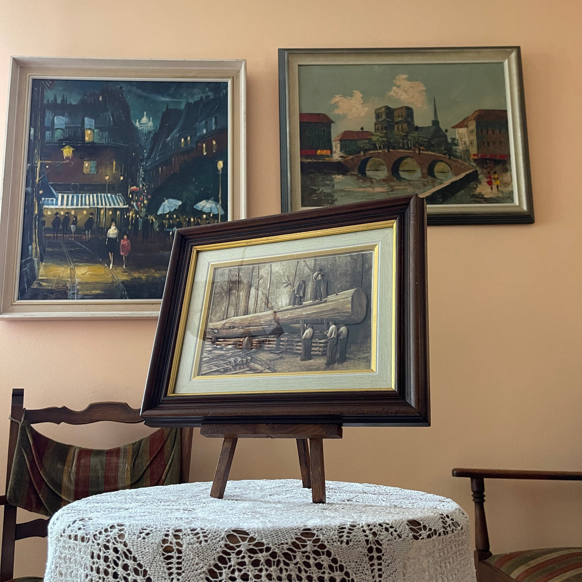 Framed artwork on a stand with other framed paintings on a wall.