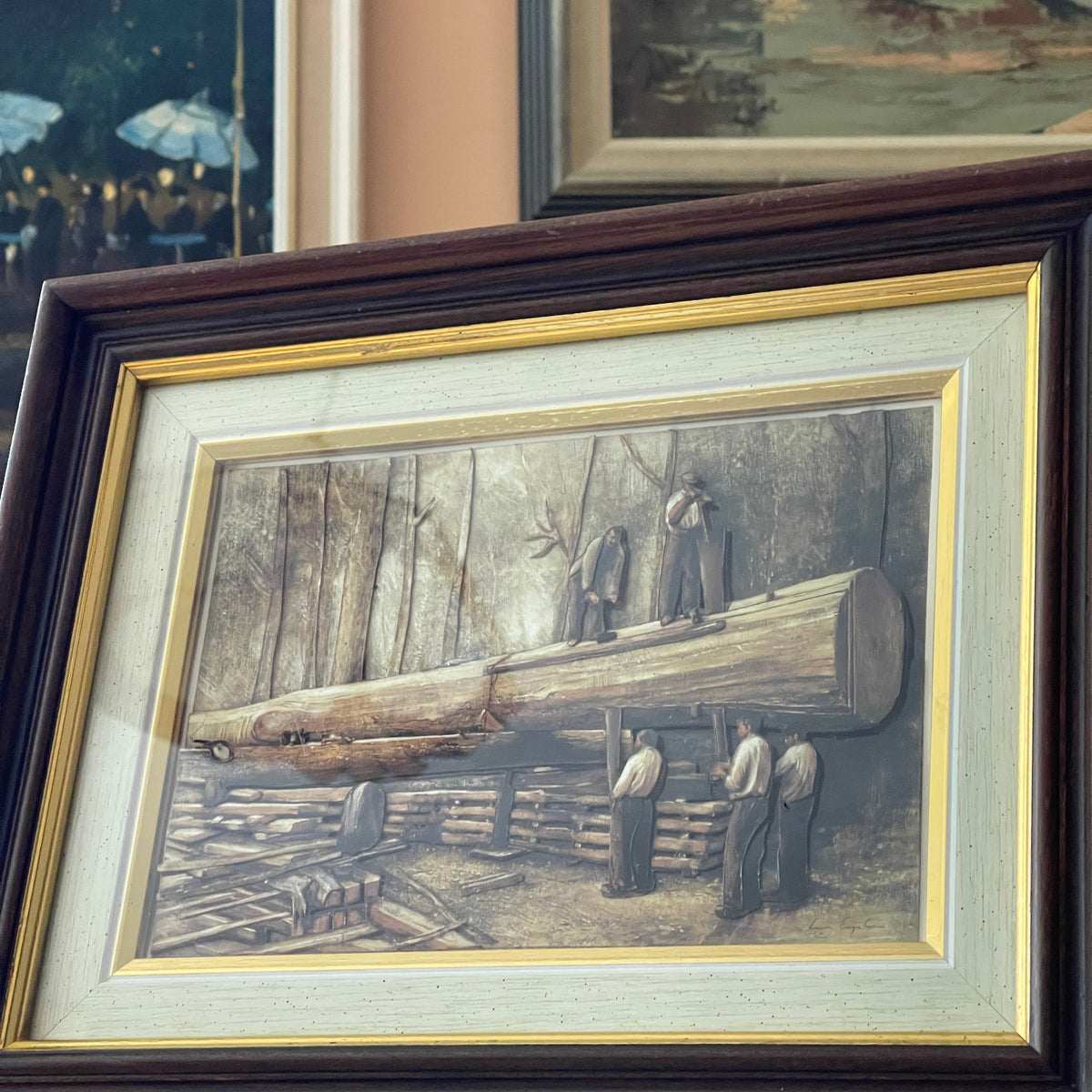 Framed artwork of a scene with people and a large log, surrounded by other framed pictures.