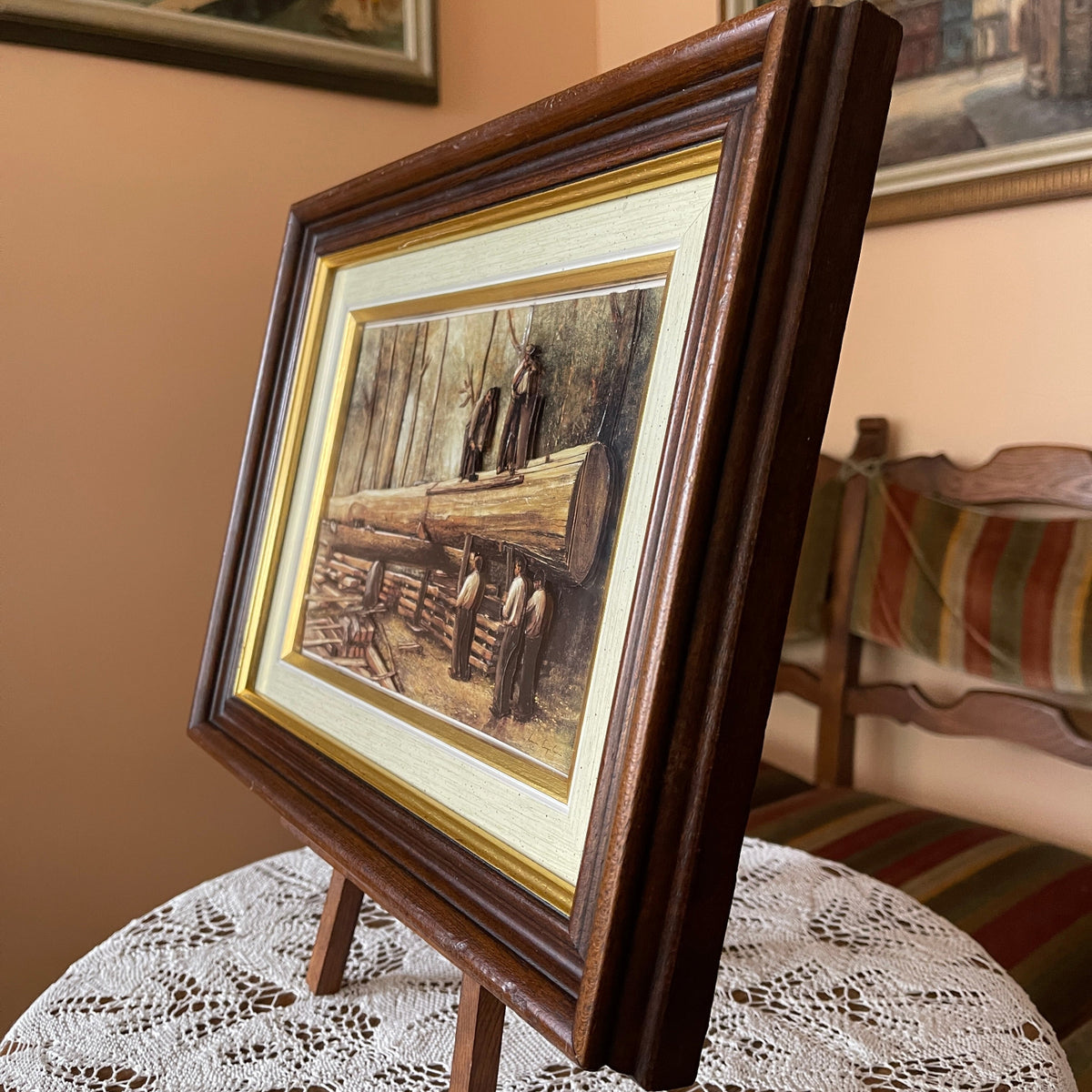 Framed artwork on a small easel with a chair and striped cushion in the background