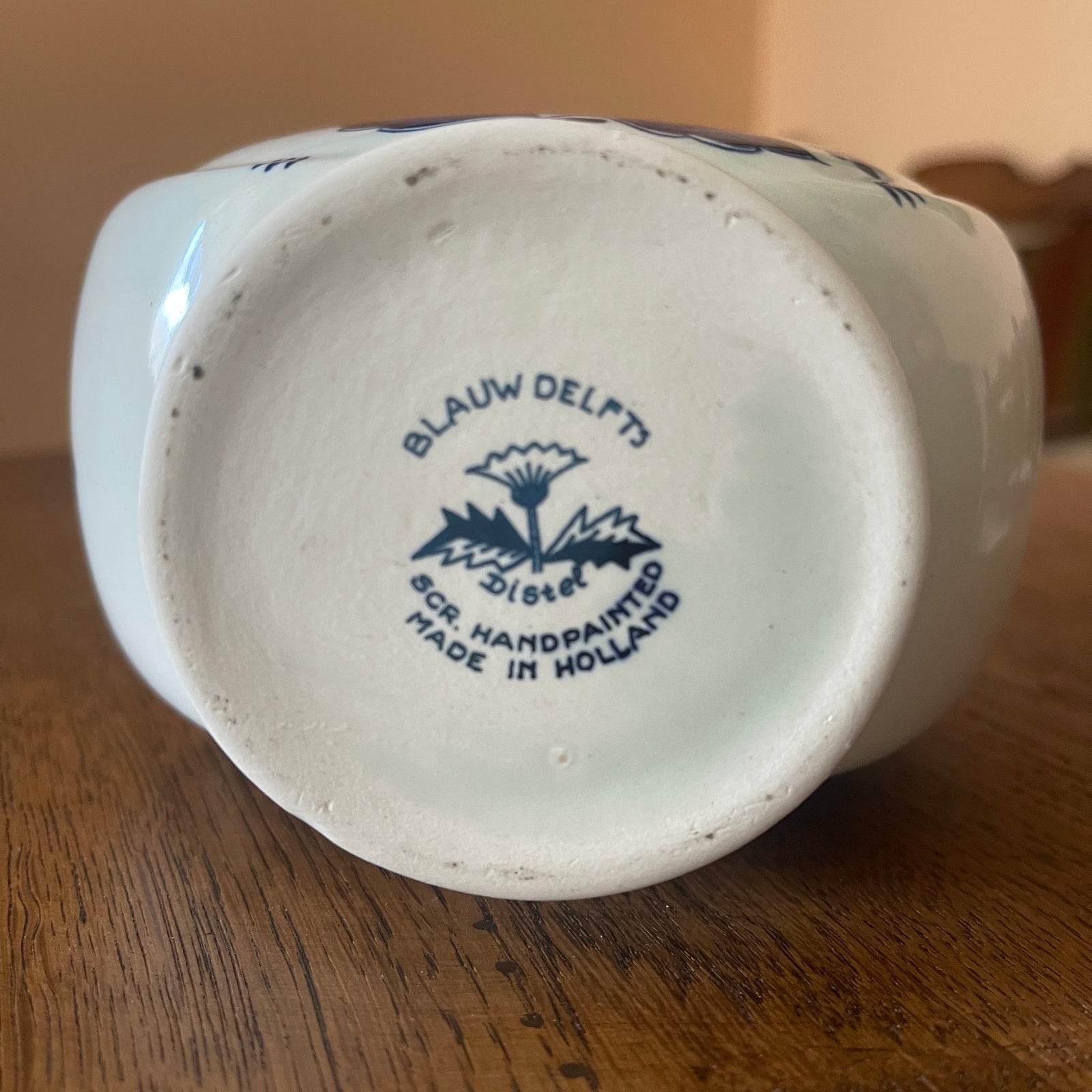 Back of a ceramic vase with 'Blauw Delft' branding on a wooden surface