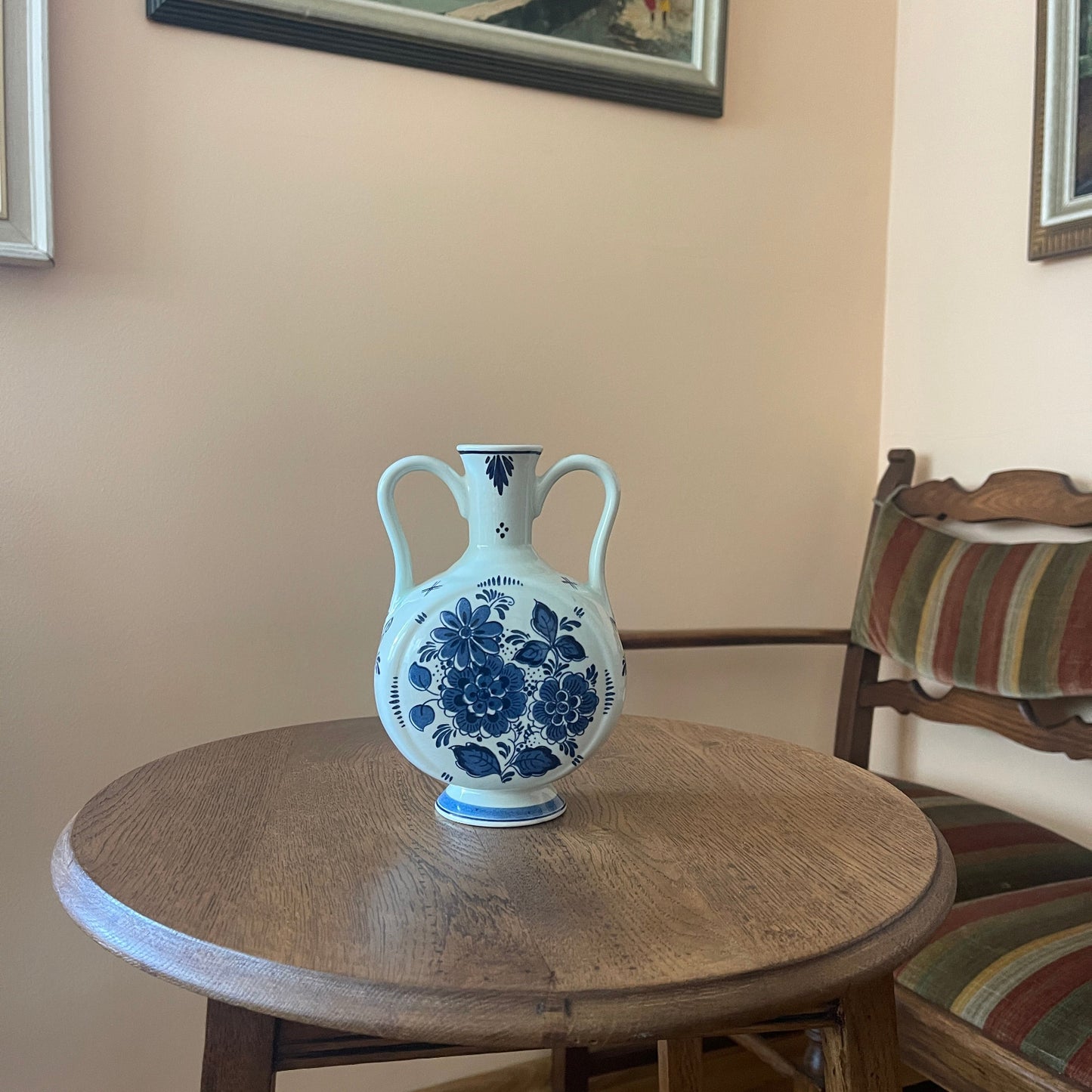 Blue and white floral vase on a wooden table with a chair and wall art in the background.