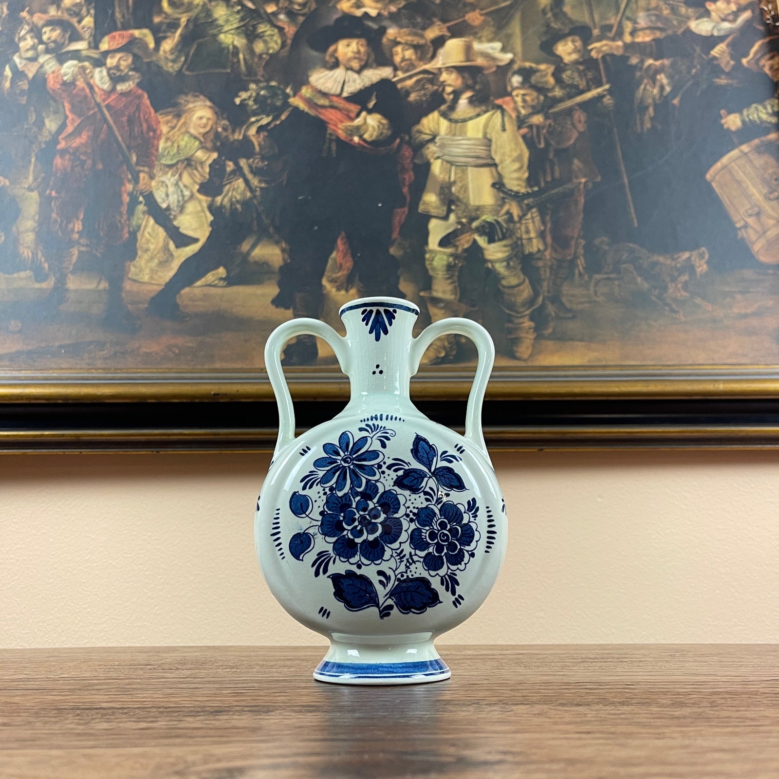 White vase with blue floral patterns in front of a painting of soldiers