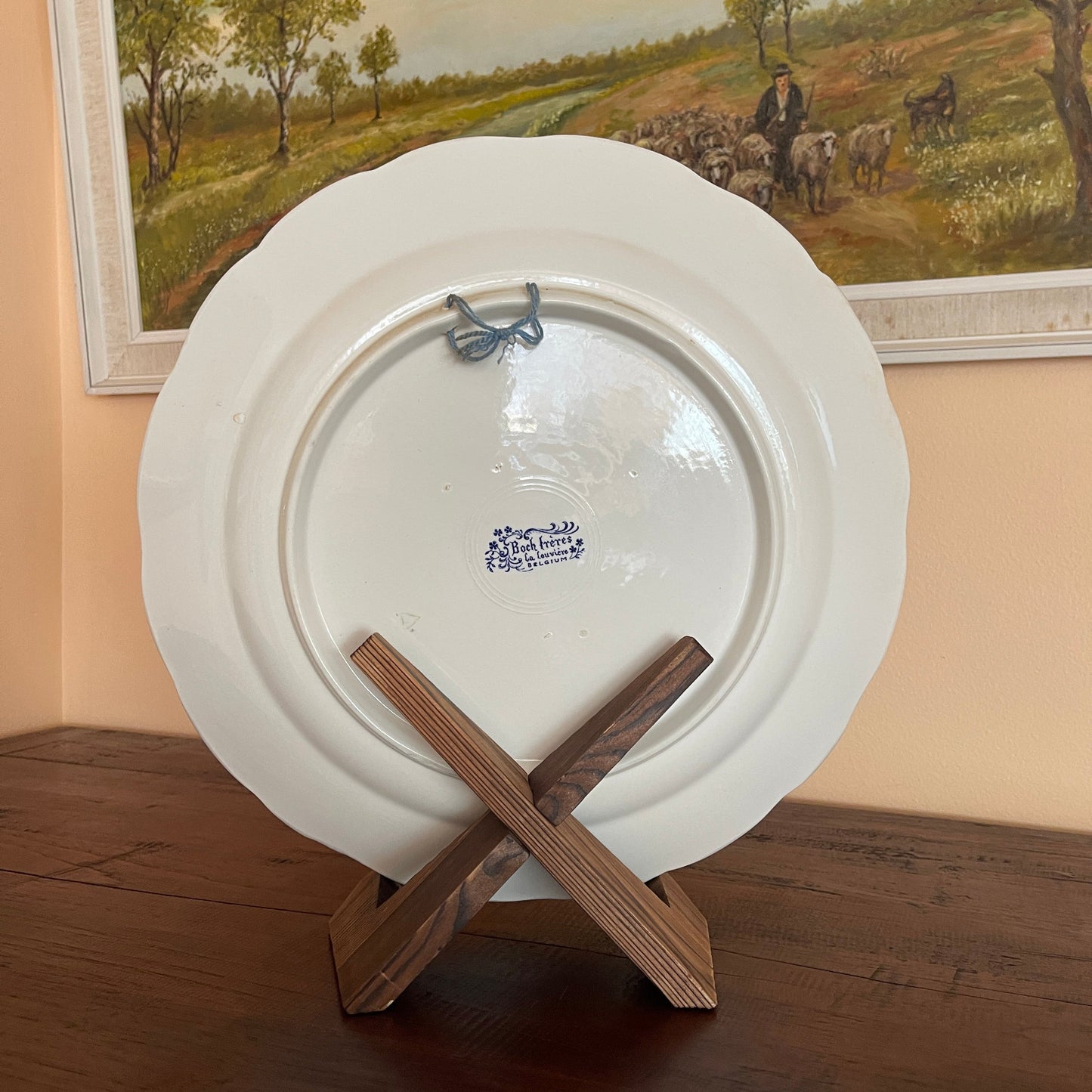 White ceramic plate with a logo on a wooden stand, framed painting in the background