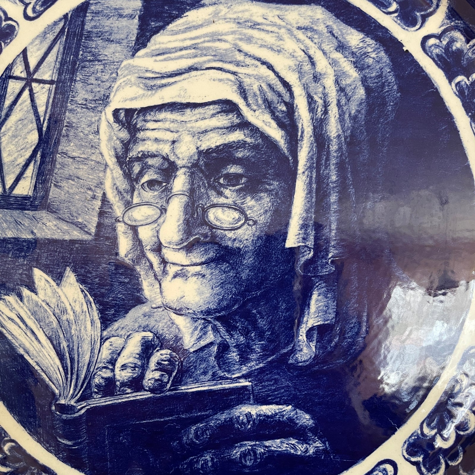 Decorative plate with an elderly woman holding a book, framed by intricate patterns.
