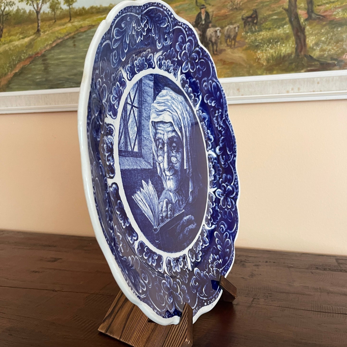 Decorative blue and white plate with a portrait on a stand, with a painting in the background.