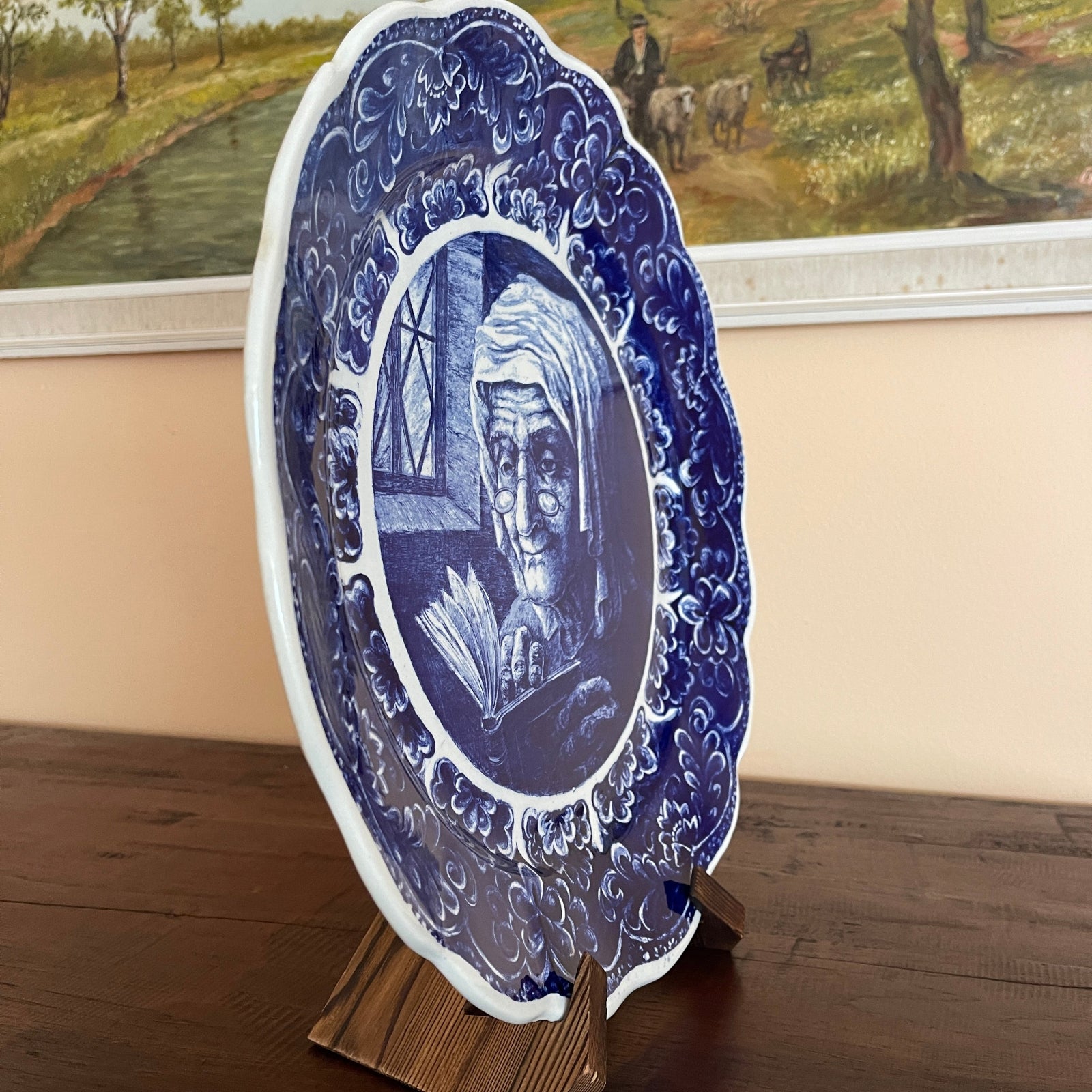 Decorative blue and white plate with a portrait on a stand, with a painting in the background.
