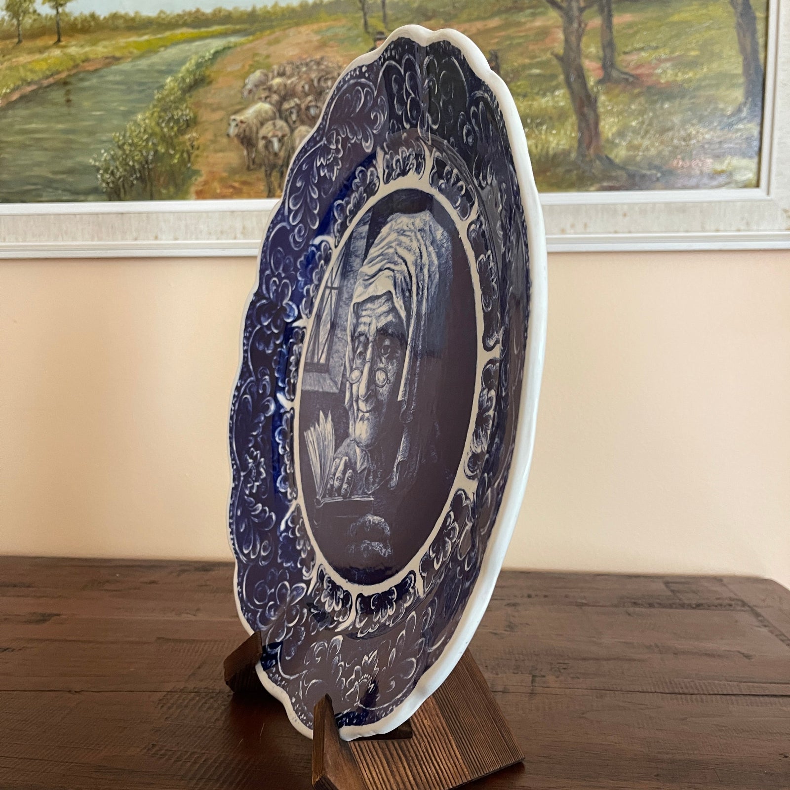 Decorative plate with a portrait on a stand in front of a scenic painting.